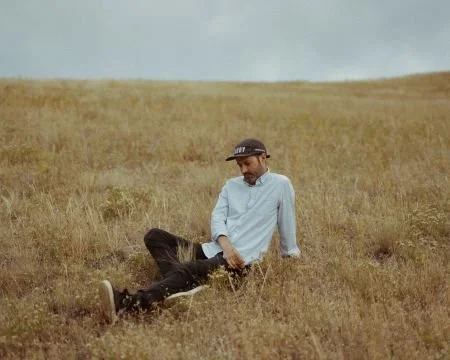 S. Carey sits in a field of dry grass, looking down