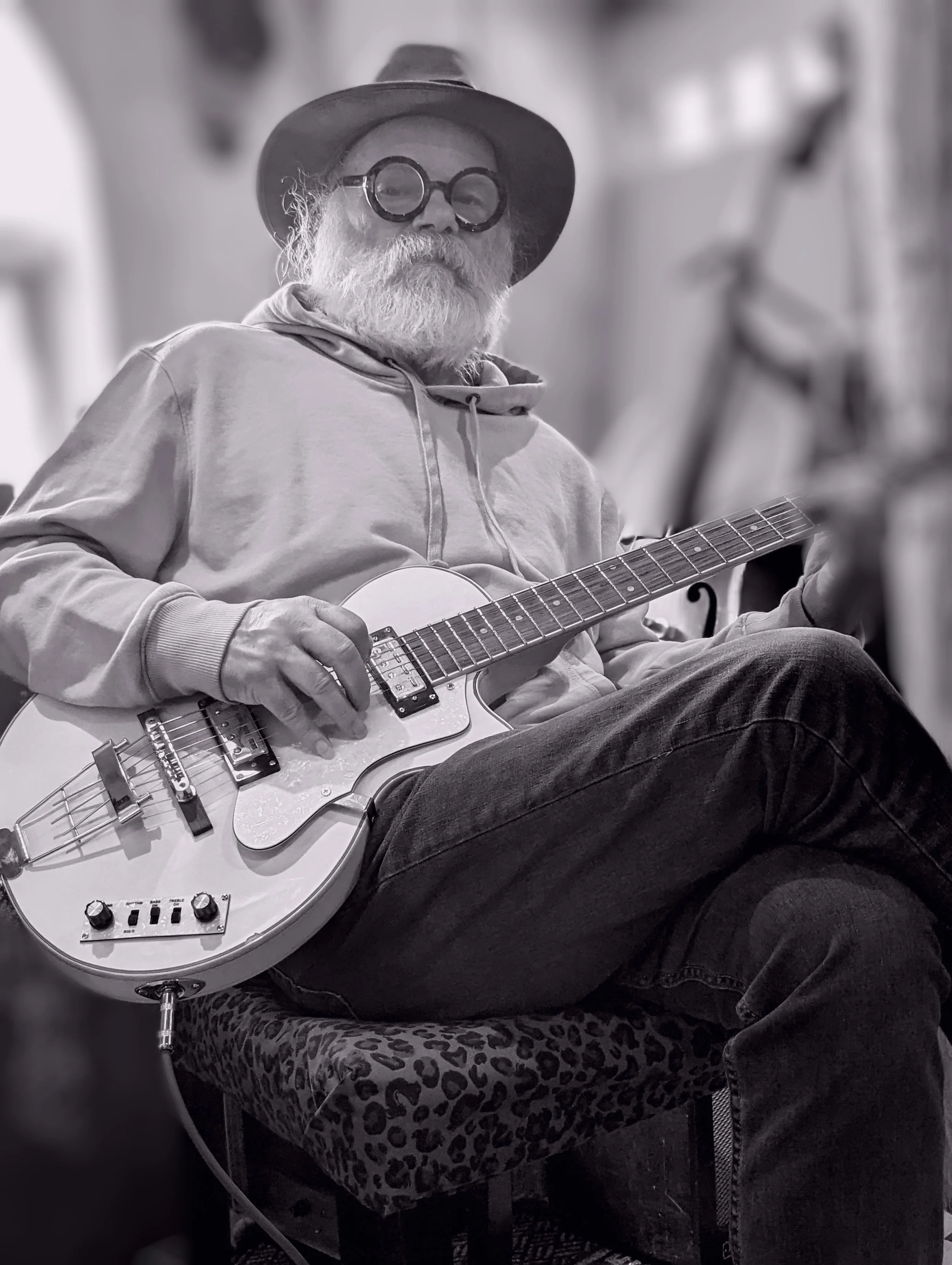 Black-and-white photo of Fred Eaglesmith seated with an electric guitar, wearing a brimmed hat and round glasses.