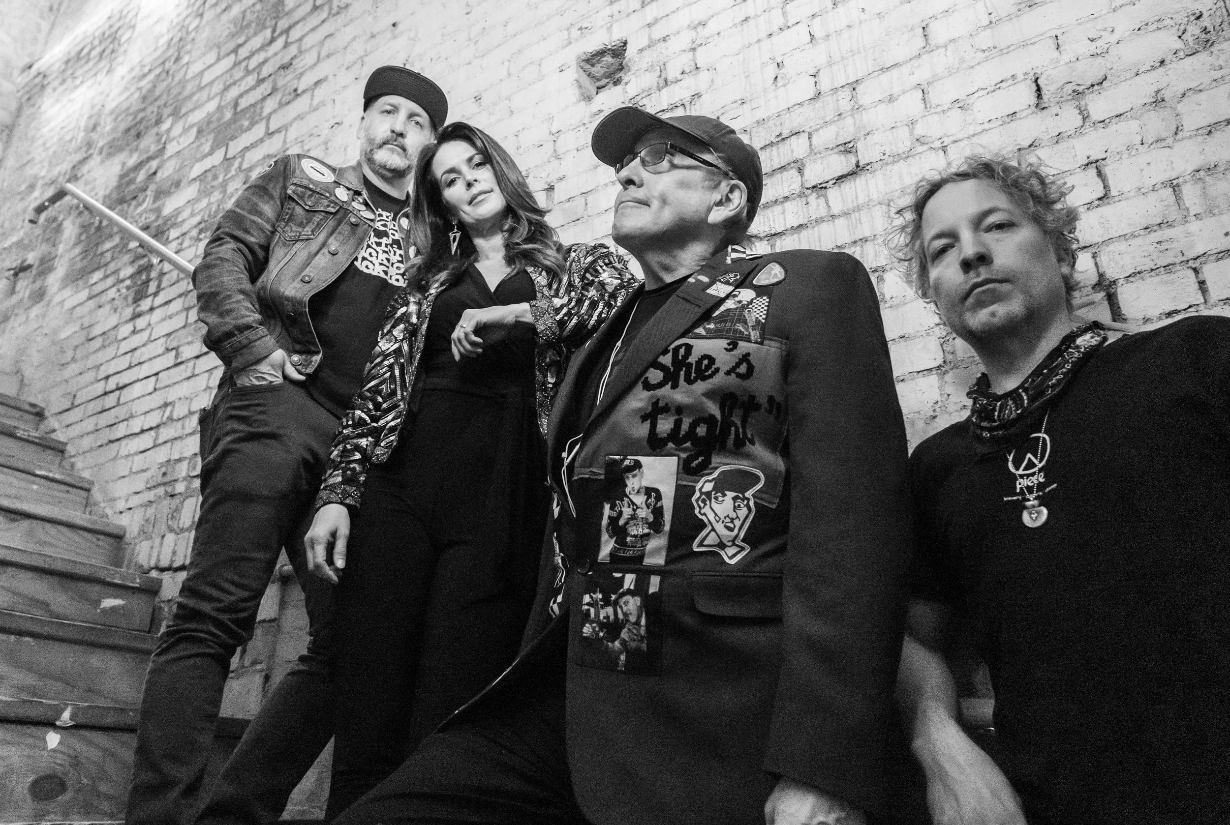 The Nielsen Trust band members pose together on a stairway against a brick wall in a black-and-white promotional photo.