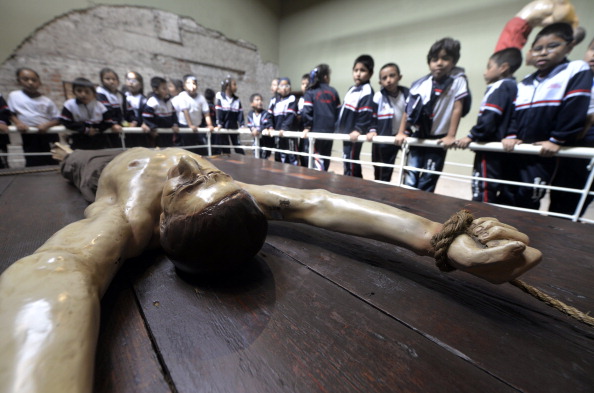 School children peer over at a wooden representation of a victim of the Inquisition in Lima, Peru. 