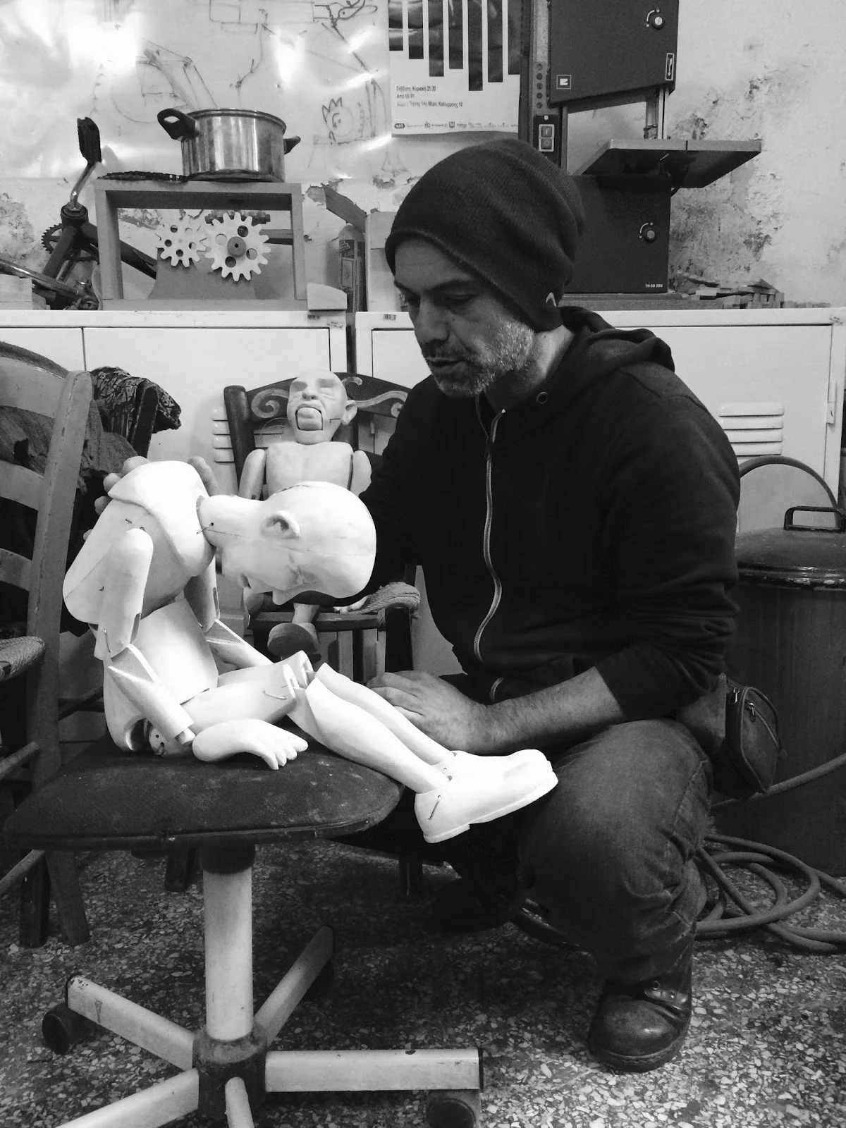 Stathis Markopoulos in the Ayusaya Workshop with wooden marionette. In the top left corner you see a pot puppet: cranking the gears below it rotates a fish puppet swimming in the pot.