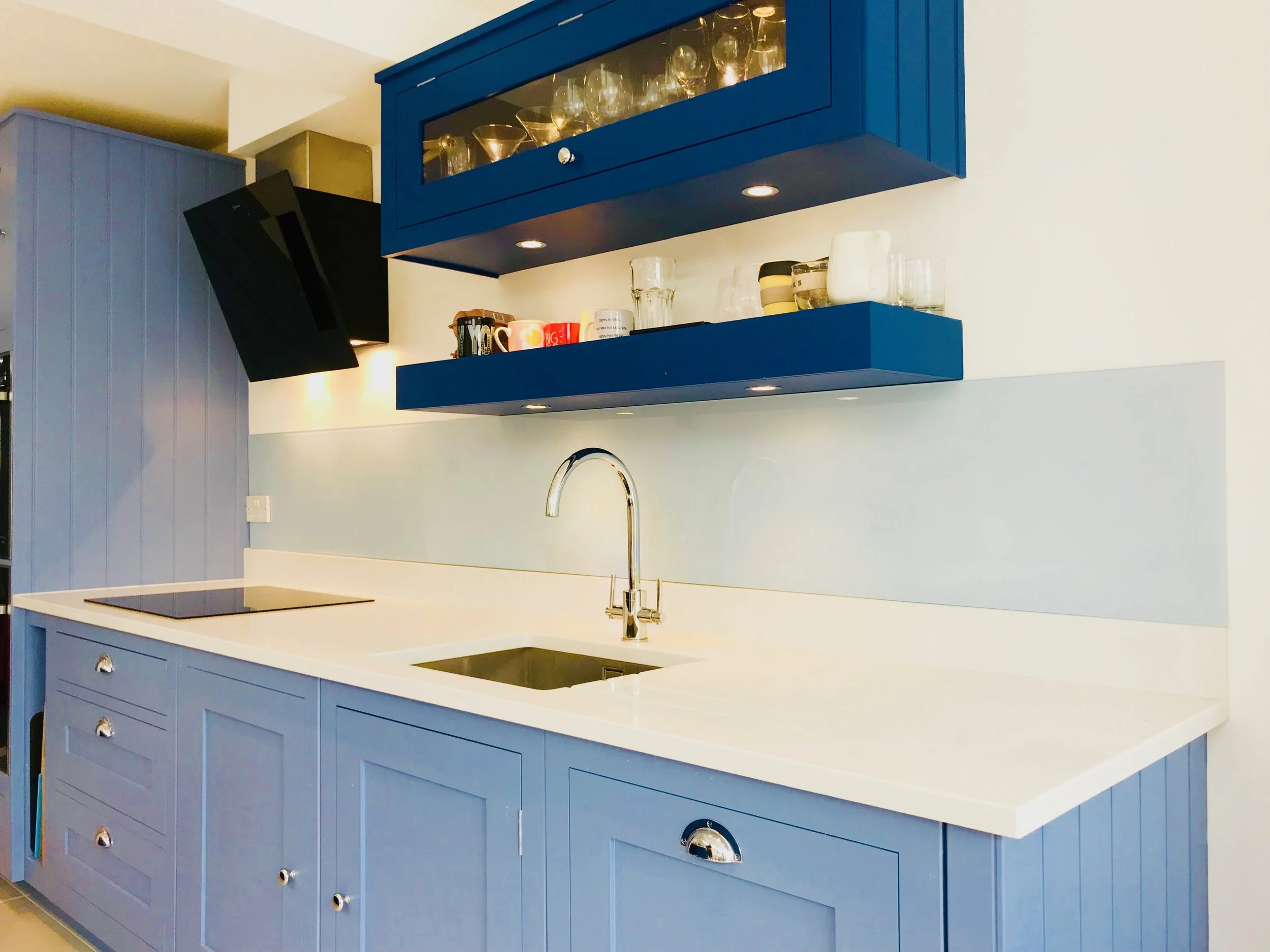 Midnight blue coloured kitchen with wall mounted storage and glass splash back
