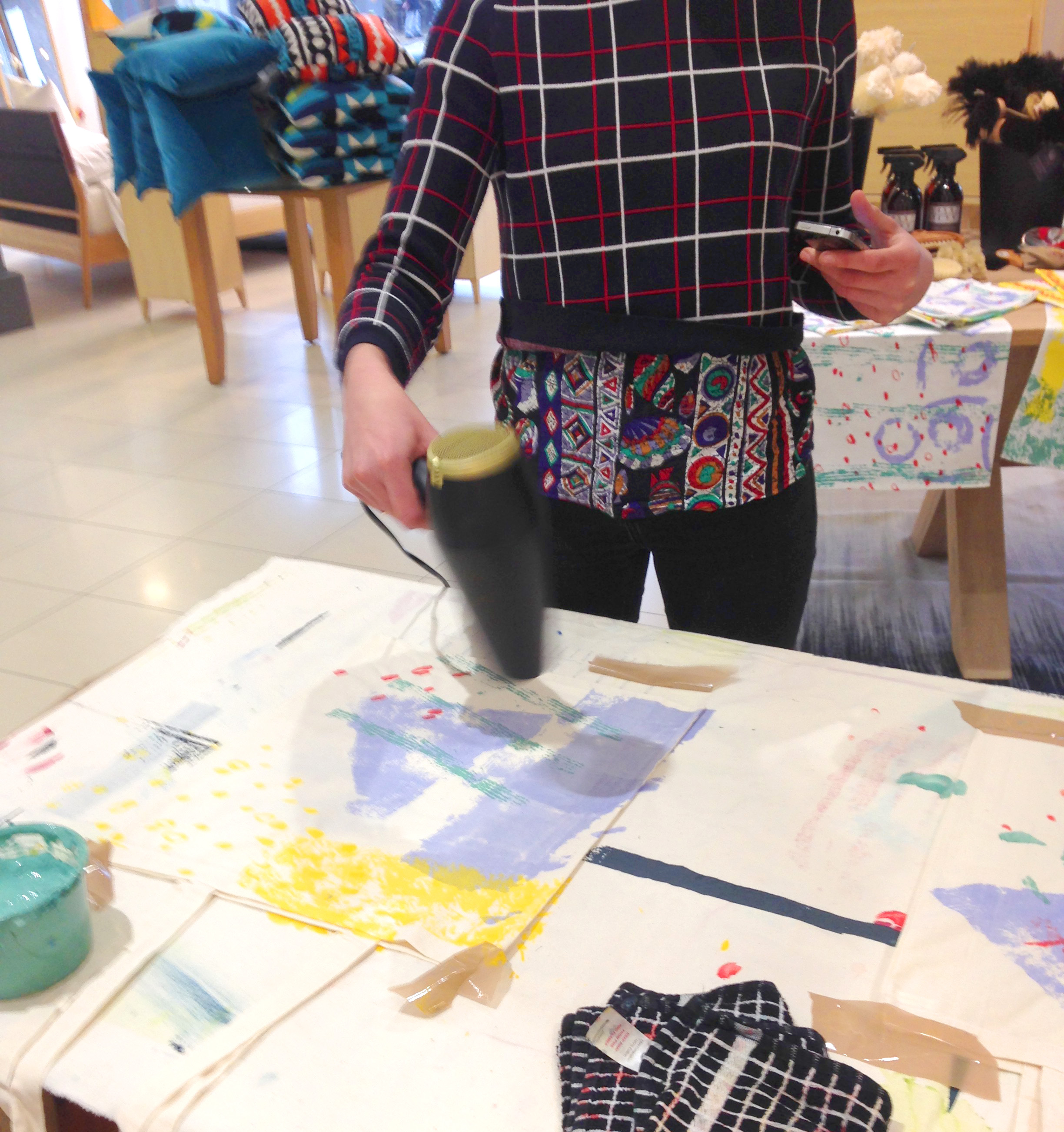Action shot with the K//M//J//C For heal's limited edition tea towels on display in the background