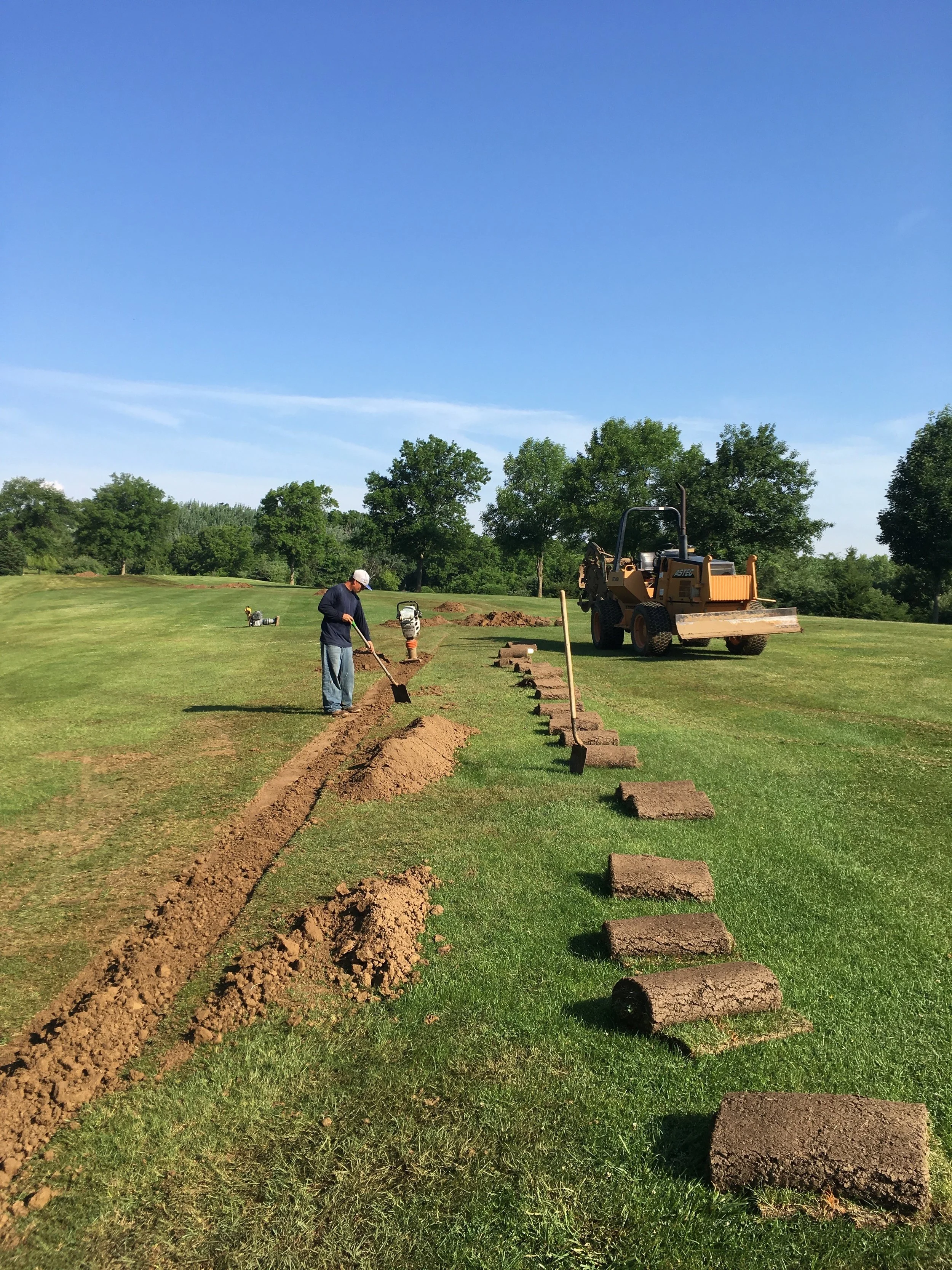 Before the irrigation pipe is trenched in, strips of sod are removed and set aside. Once the pipe is placed in the trench, workers cover it with dirt, then replace the sod.