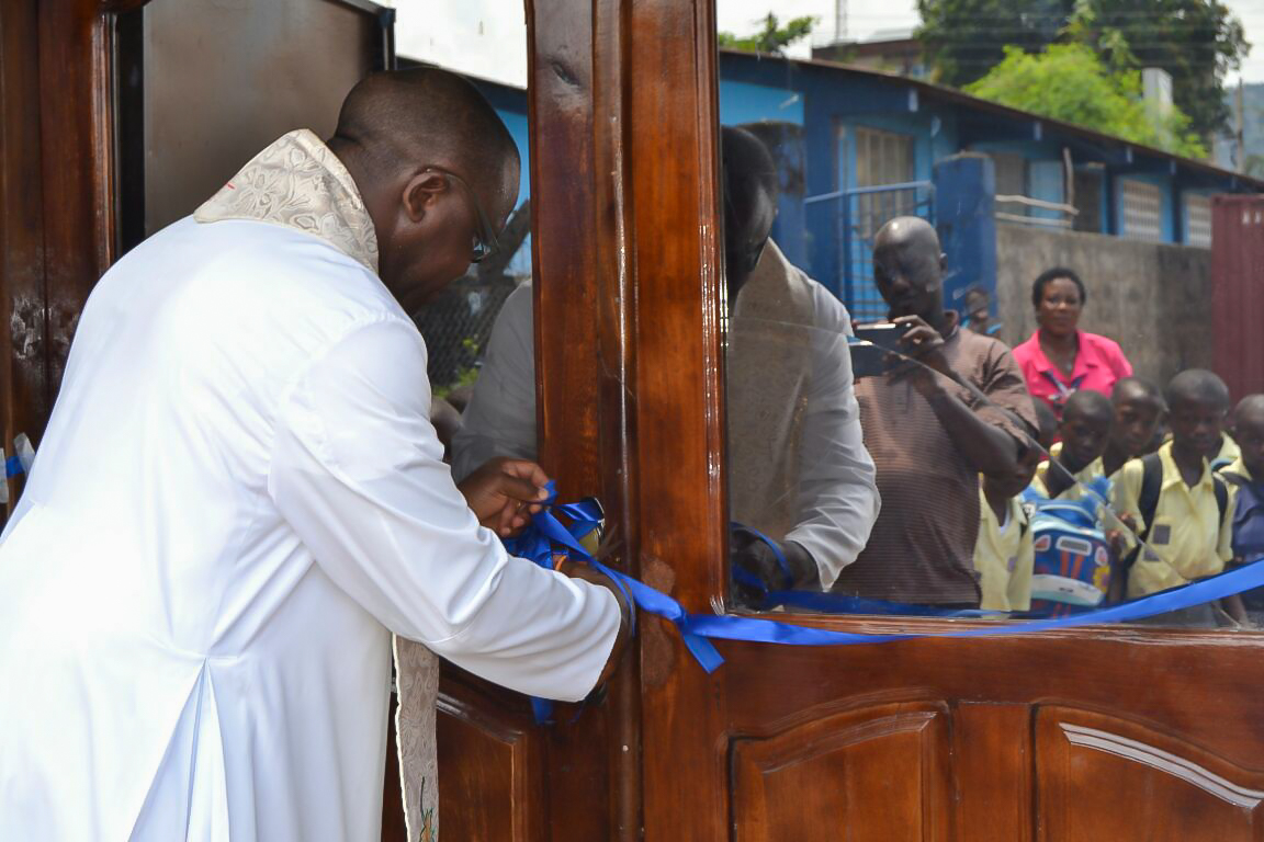 Father Bassey cutting ribbon at dedication for Hope for Lives at St. Anthony's Computer Lab