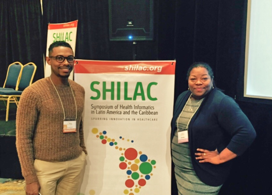 Research Associates Christopher Cross and Latifa Jackson pose in front of the SHILAC poster.