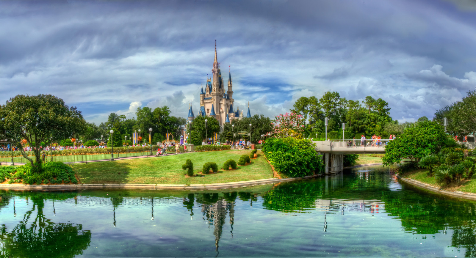 As I walk around a subject like this that is so central to the design aesthetic of the landscape, I find myself looking at it from every vantage point to try to find the ideal location to capture it. In this case, the ideal location appeared to be from within a roped off section of seating on the path between main street and tomorrow land that runs near the smoking section right against the moat, as soon as you turn right off of Main Street. Because the restaurant here is closed, this is apparently a seating for special viewing of the fireworks display over the castle.
I ducked the DO NOT ENTER sign and captured this with my tripod. Actually, it is 9 shots in all, 3 sets of three in a panoramic that is closely cropped. The water is a little dingy in this area but the reflection in the sky helped to downplay the algae growing there. Probably my favorite Castle shot because of the added width to include the tree. I'm certain a good wide angle would have been able to do the same.
from the Photoblog: www,graffitivisuals.com