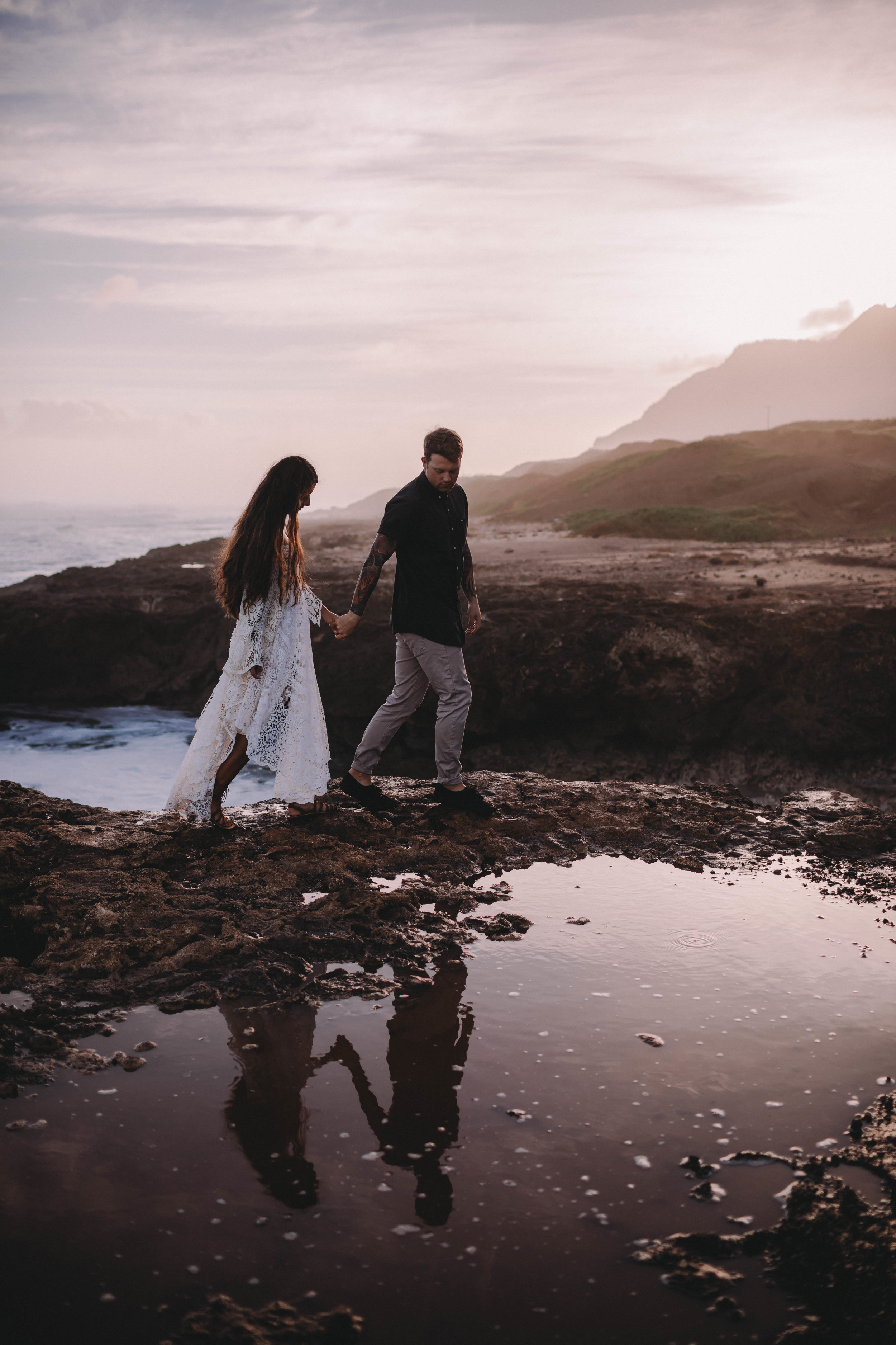  couple on a sea cliff in hawaii with their reflections shown in a tide pool  