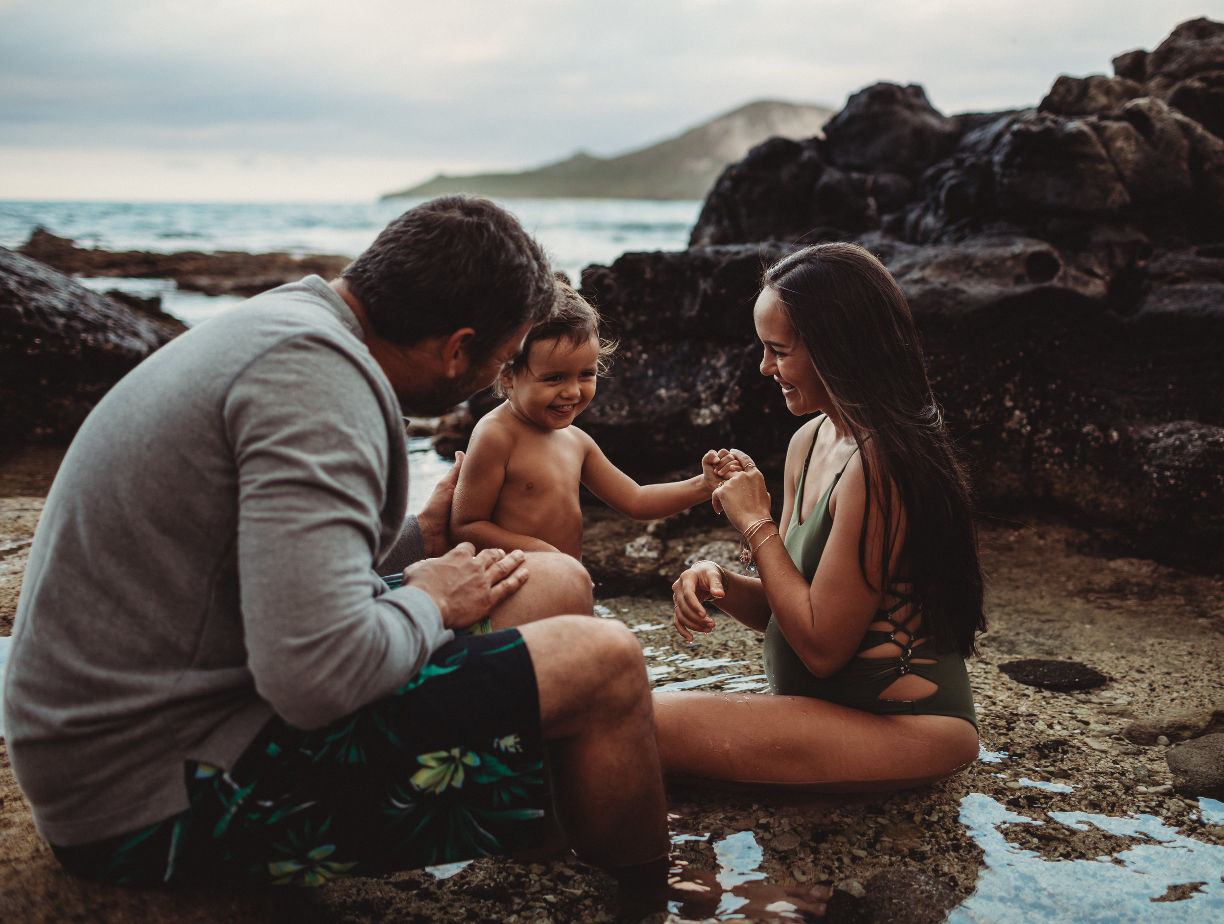  mom and dad smiling at their toddler in a tide pool in hawaii 