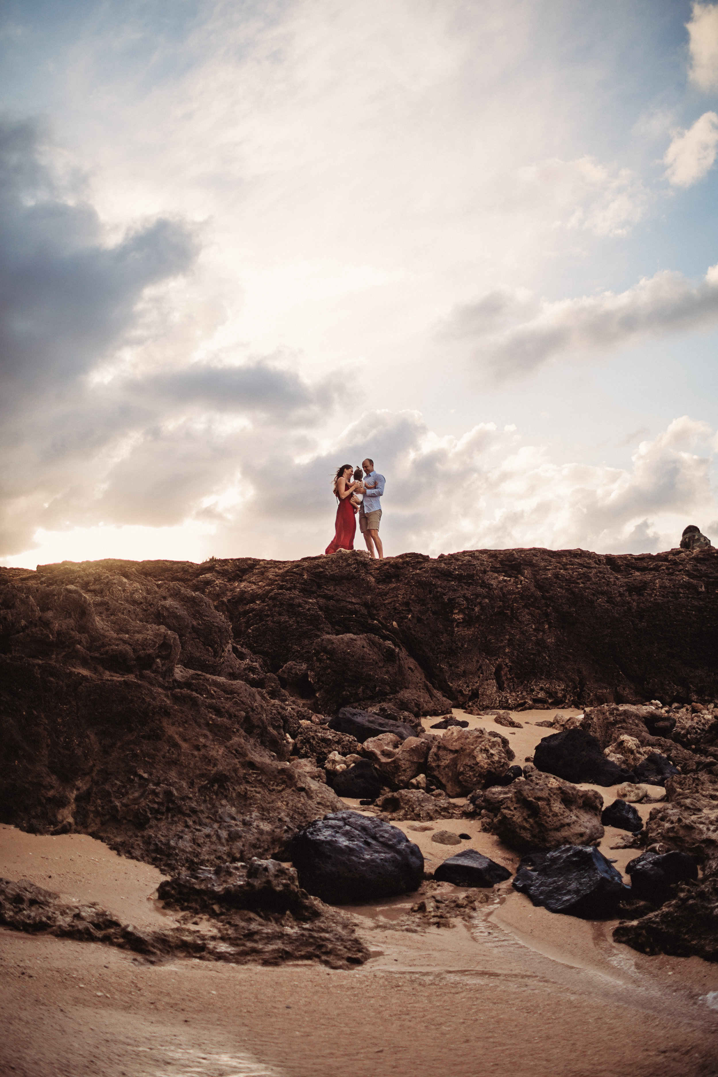  family of three standing on a rock cliff near a beach in hawaii  