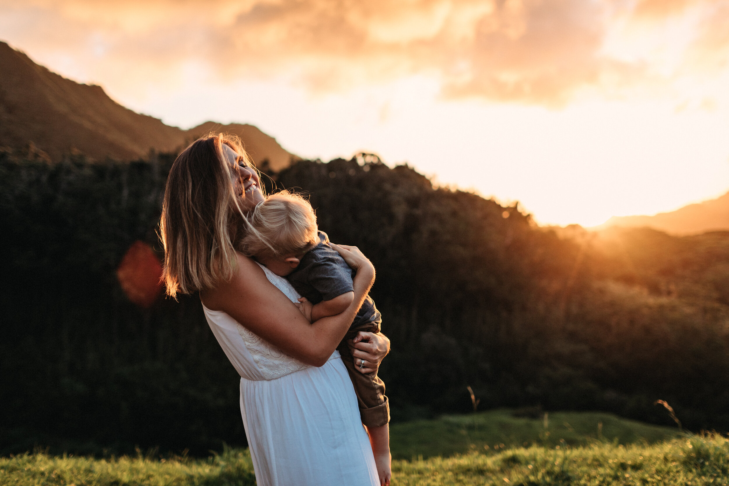  mother holding her child with mountain and sunset behind them 