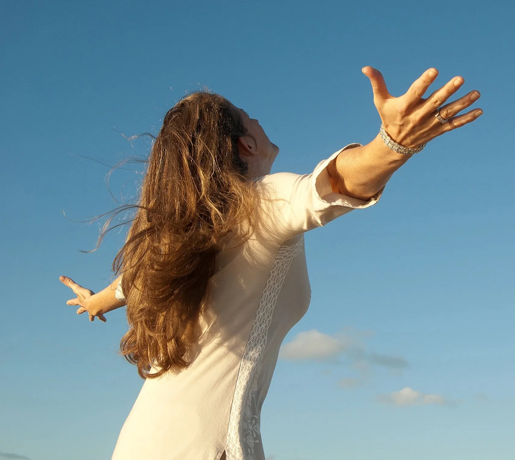 Woman with long wavy hair reaching out with her arms against a clear blue sky. Dallas therapist Dr. Jada Jackson offering therapy and wellness support.