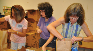 Junior Auxiliary of Taney County members, from left,Brenda Galyean, Donna Harris and Cathy Brown, pack brown paper sacks with ready-to-eat meals, snacks, shelf-stable milk and juice at Hollister Elementary School Thursday evening. Each week, 125 sacks of food will be given out to Hollister students identified as possibly not having enough food to eat.