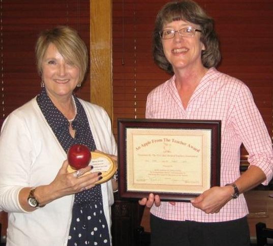 Cathy Brown (right), President of Junior Auxiliary, accepts the Apple from the Teacher award from Evelyn Layton, Vice President of Tri-Lakes Retired Teachers.