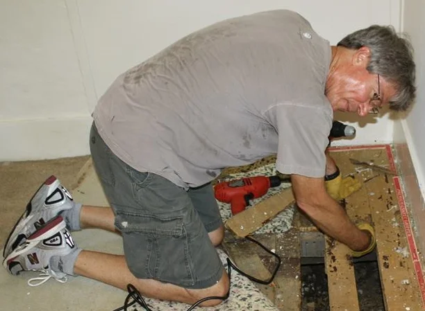 Clark Harris replaces rotten floorboards before new carpet is installed.