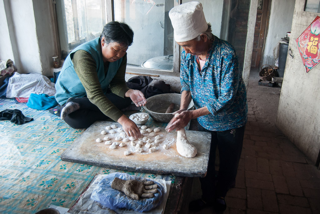 I make the hands in each family's home. As I am mixing soil, the women are kneading dough, preparing our meal. In July 2011, while a rough draft of her hand dried on the kang, Zhang Shuzhi (right) and a visiting neighbor rolled out dough for steamed pork dumplings.