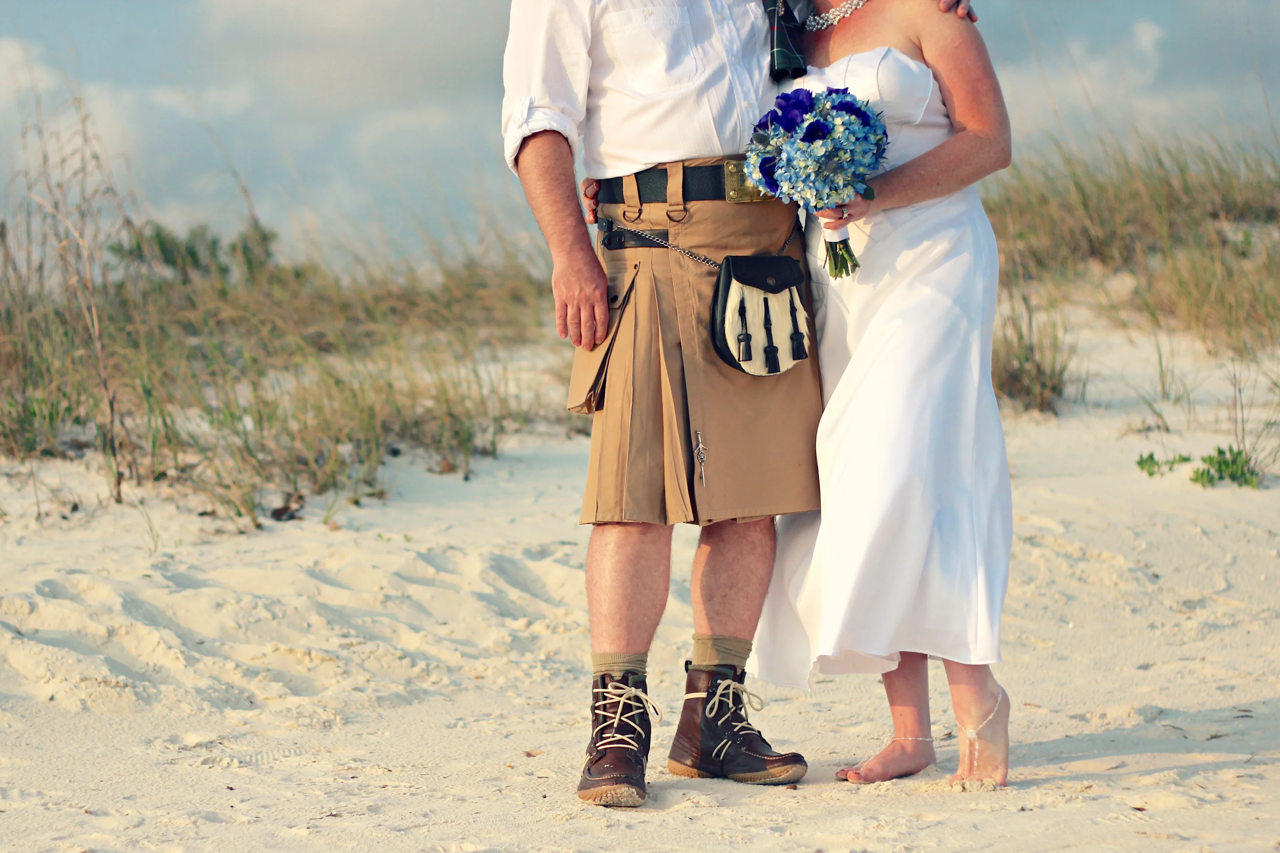Wedding portrait of bride in dress and groom in kilt with sand dunes on Biloxi Beach