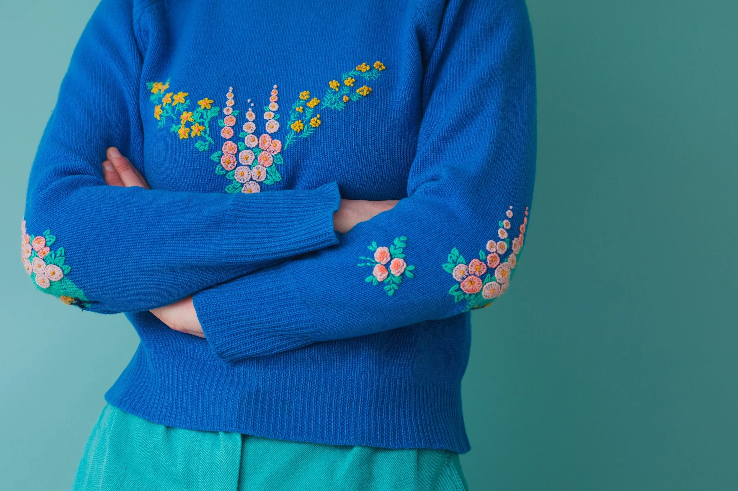 Close up shot of designer Flora Collingwood-Norris wearing a cobalt blue jumper that has been visible mended with floral embroidery stitches