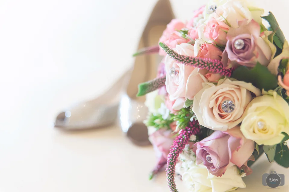 Close-up of a pastel-colored bouquet of roses with some jewel embellishments and a glittery silver shoe in the background.