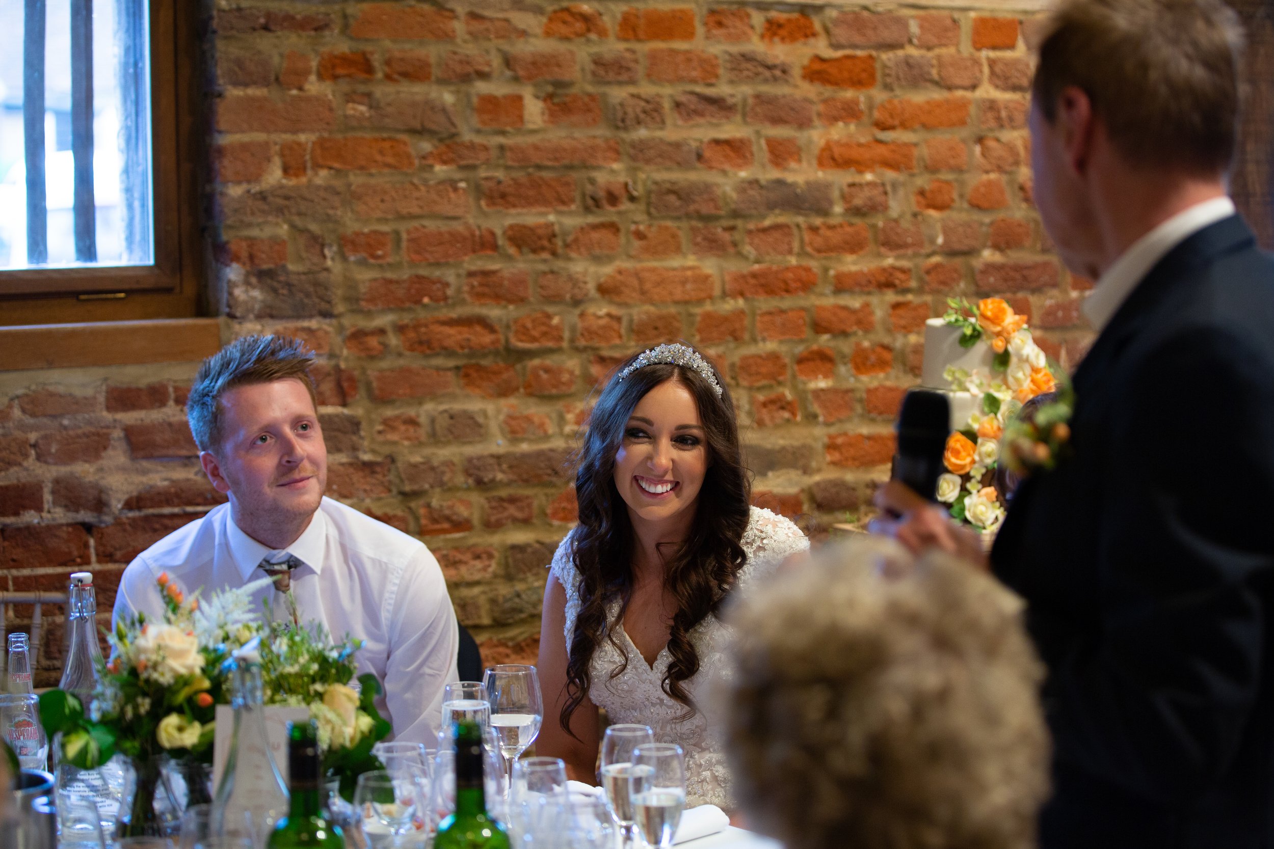 Bride and groom listening to best man giving a speech at their wedding reception.
