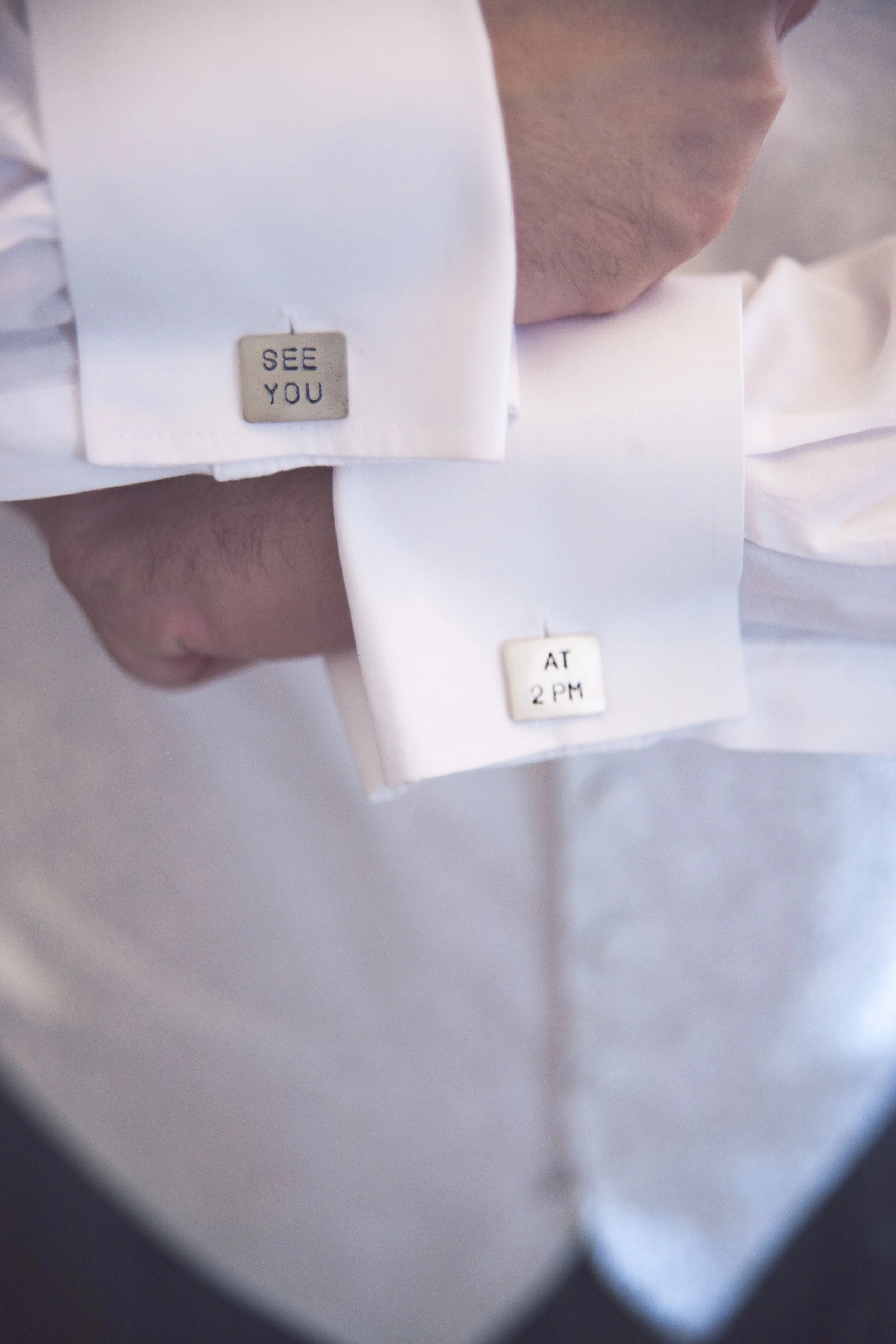 Cufflinks on a white dress shirt, one with the words 'SEE YOU' and the other with 'AT 2 PM'.