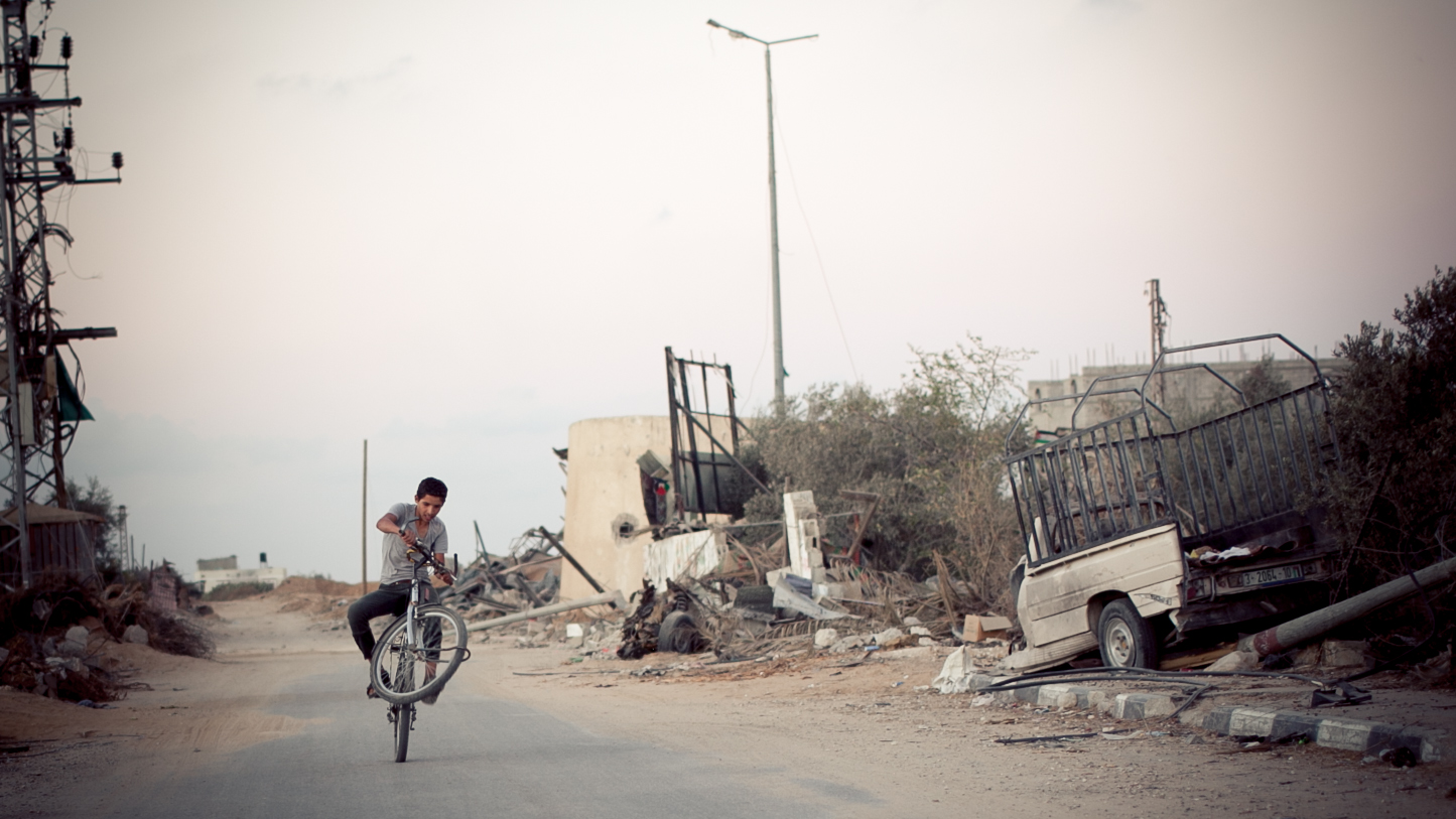 A young man rides his bicycle through Khuza'a in Khan Yunis. Sixty percent of homes were destroyed and two thirds of the residents were left homeless. (Tyson Sadler)