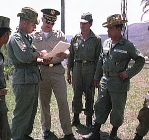 Foto de una película del ejército Estadounidense rodada en 1965. Los asesores militares de Estados Unidos se reúnen con el coronel Carlos Arana Osorio y un ayudante observa. De izquierda a derecha: el sargento Casper González, asesor de infantería EE.UU, el asesor de inteligencia del Ejército de EE.UU Mayor Vernon Justice, un soldado guatemalteco no identificado, y el coronel guatemalteco Carlos Arana Osorio . Photo still from U.S. Army film shot in 1965. U.S. military advisors confer as Col. Carlos Arana Osorio and an aide look on. From left to right: Sgt. Casper González, U.S. infantry advisor; U.S. Army intelligence advisor Major Vernon Justice; unidentified Guatemalan soldier; and Col. Carlos Arana Osorio.