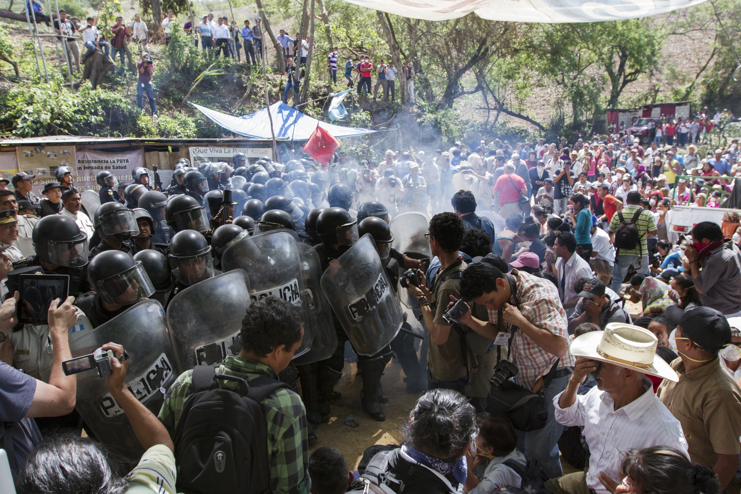 Después de dos años y dos meses de bloquear pacíficamente la entrada a la mina de oro El Tambor de la compañía estadounidense Kappes, Cassiday & Associates (KCA), miembros de la resistencia de La Puya fueron violentamente desalojados por agentes de la Policía Nacional Civil que apoyaron el ingreso de maquinaria pesada. Liderados por mujeres que rezaban y cantaban, miembros de la resistencia finalmente fueron desalojados por medio de gas lacrimógeno. Varias personas resultaron heridas o detenidas. Foto: James Rodríguez After two years and two months of peacefully blocking the entrance to U.S.-based Kappes, Cassiday & Associates (KCA) El Tambor gold mine, local residents of San Jose del Golfo and San Pedro Ayampuc were violently evicted by Guatemalan Police forces in order to introduce heavy machinery inside the industrial site. Led by the local women, members of the La Puya resistance prayed and sang until they were faced with tear gas. Numerous locals were injured and detained. Photo: James Rodríguez.
