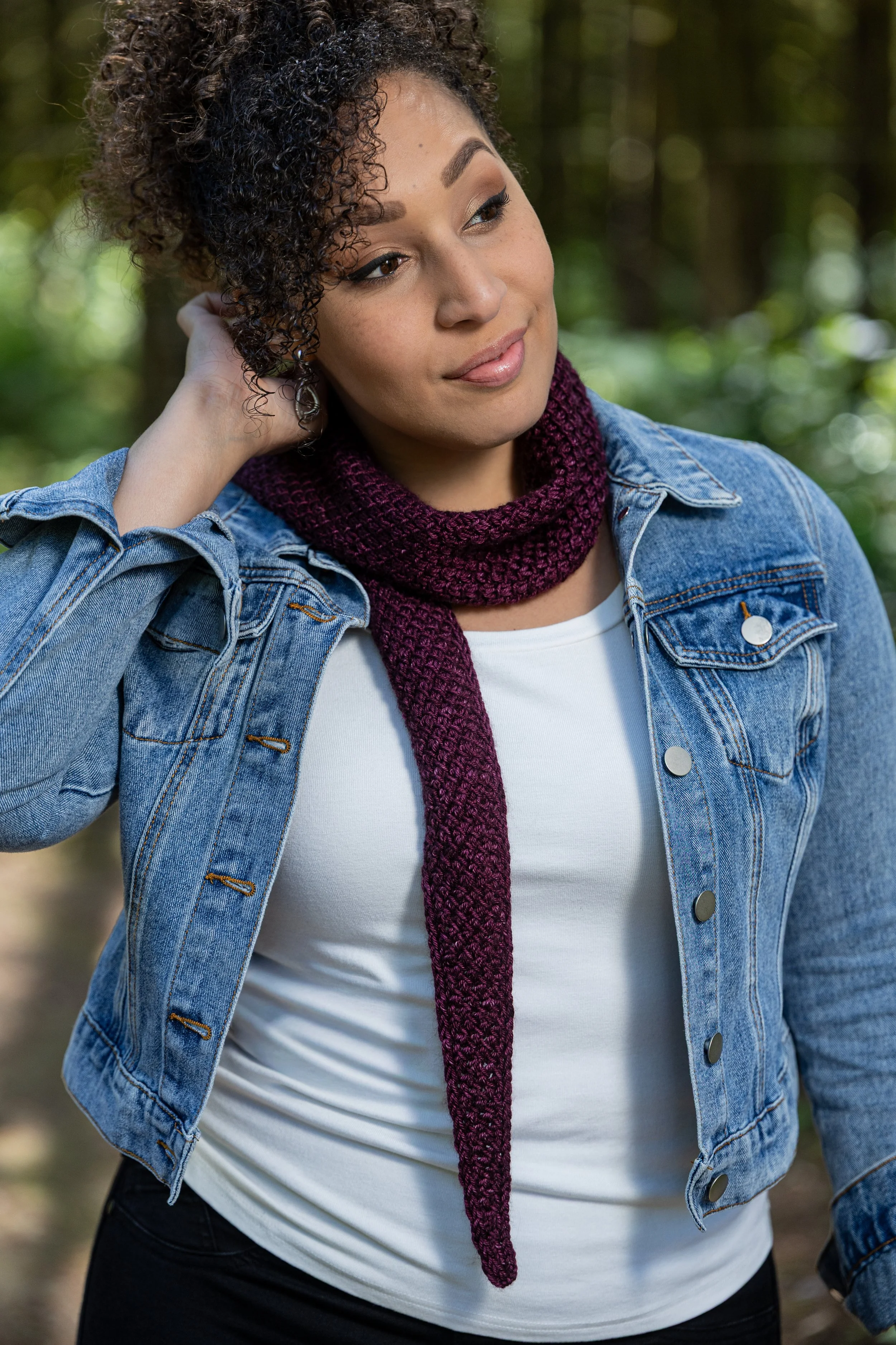 BIPOC designer Vanessa Smith casually wears semisolid, burgundy skinny scarf knit from tip-to-tip using shallow triangular shaping and at-the-same-time i-cord edging. A beautiful, one-skein gift idea.