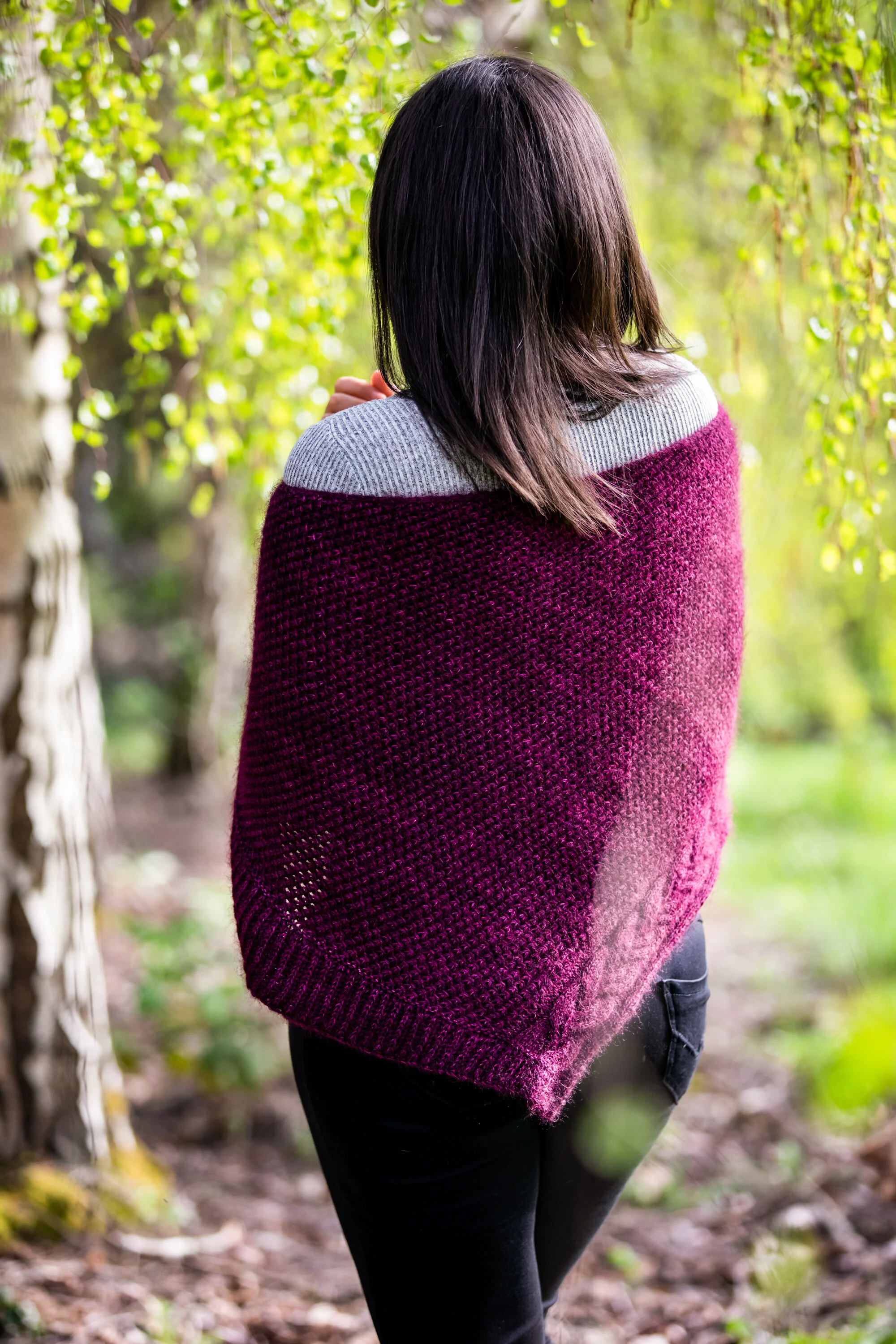 Back view of the hand-knitted Indira Shawl in tonal, hand-dyed purple yarns held double, highlighting its graceful shaping and cable & lace detail. PDF knitting instructions by Vanessa Smith Designs.