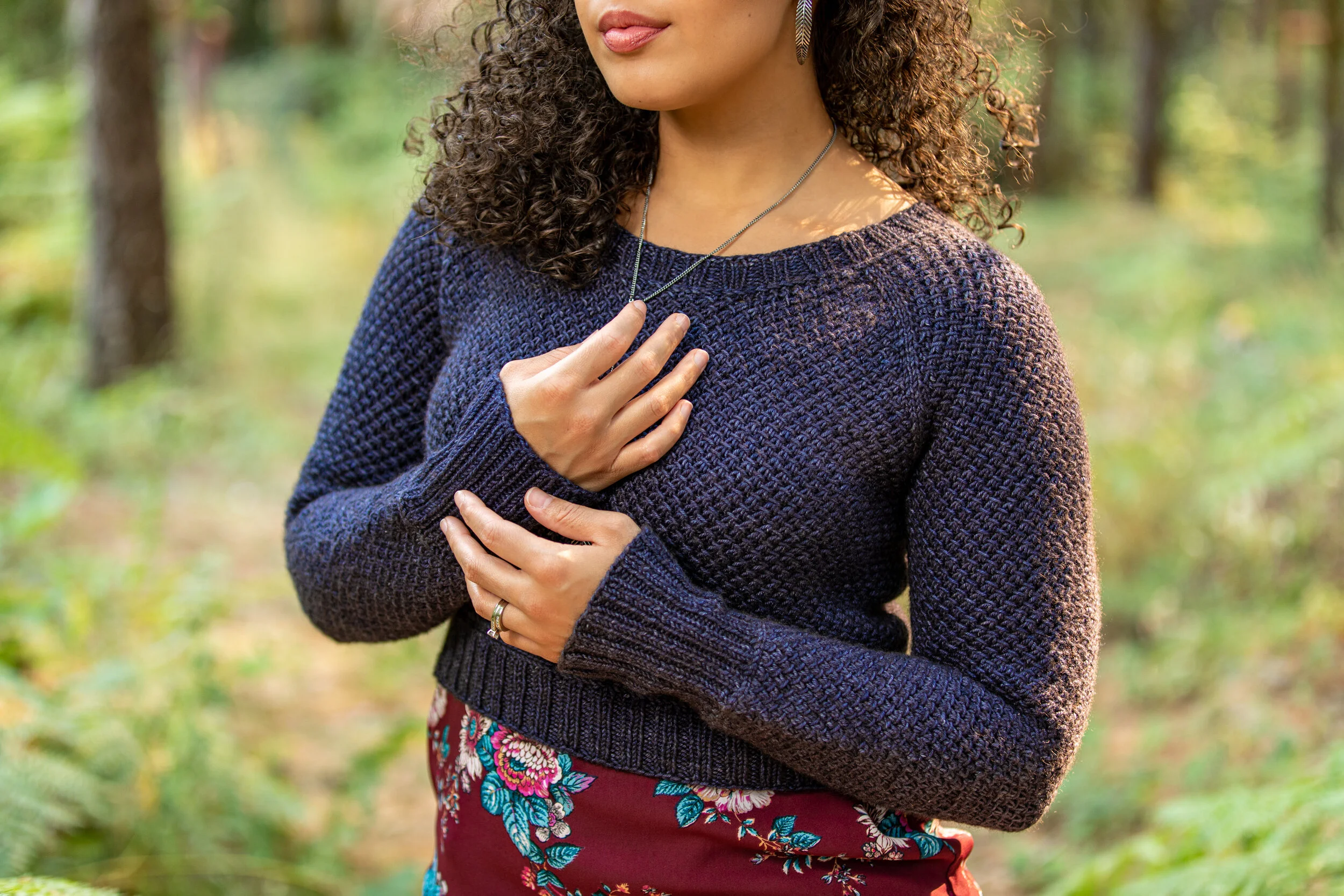 A biracial, curly-haired woman wears the close-fitting Nydia sweater, a top-down, seamless raglan knitting pattern designed with care for petite and plus-sized women alike. Paid, instant PDF download.