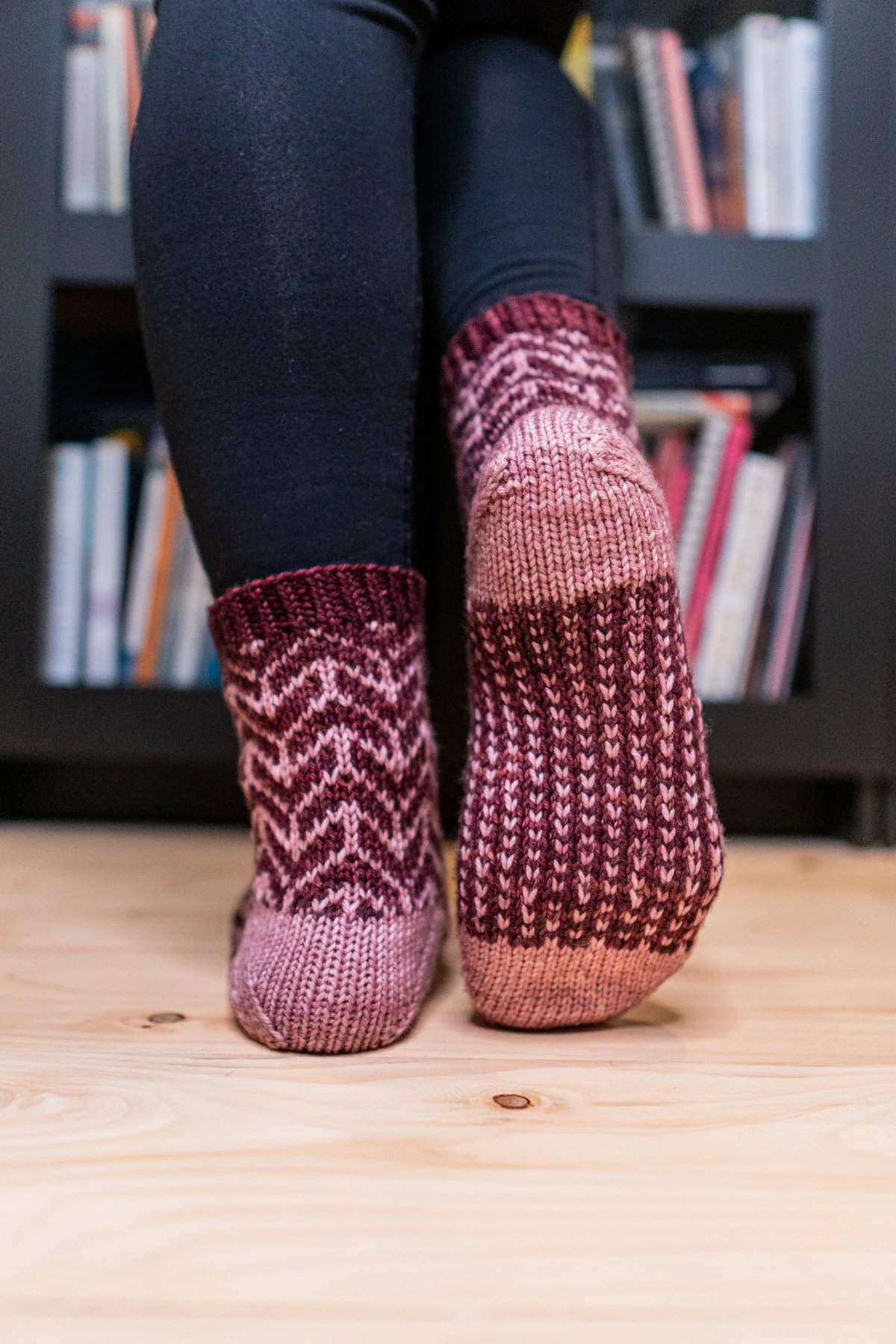 Back view of the Kestra Socks pair, highlighting the forethought/afterthought heel in a contrasting color and the different stranded colorwork stitch patterns. PDF knitting pattern by Vanessa Smith.