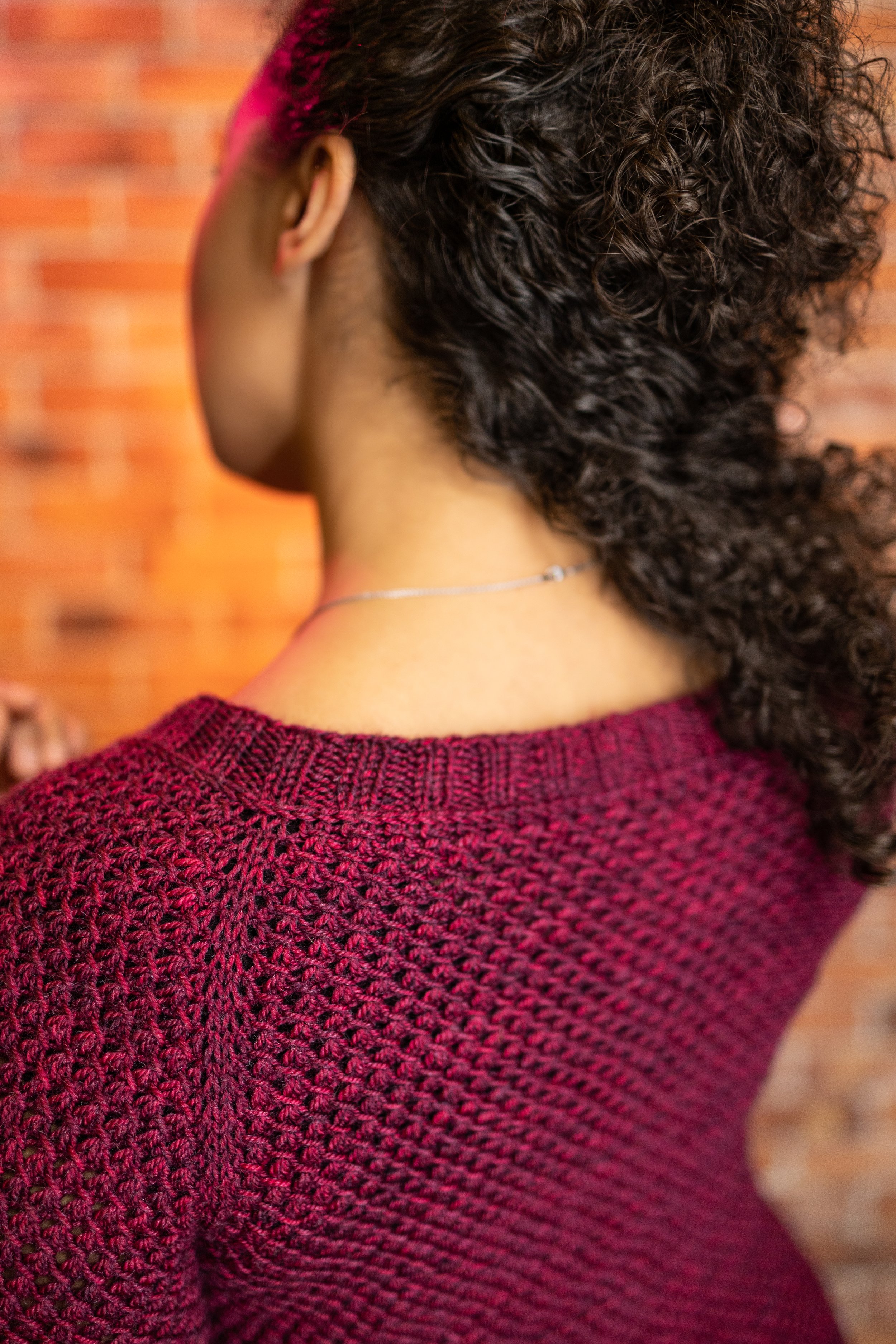 Detailed closeup of the back neckline ribbing, lateral braid detail, and raglan shaping on the top-down Nydia Cardigan worked in DK weight yarn. Inclusively sized women's knit pattern by Vanessa Smith