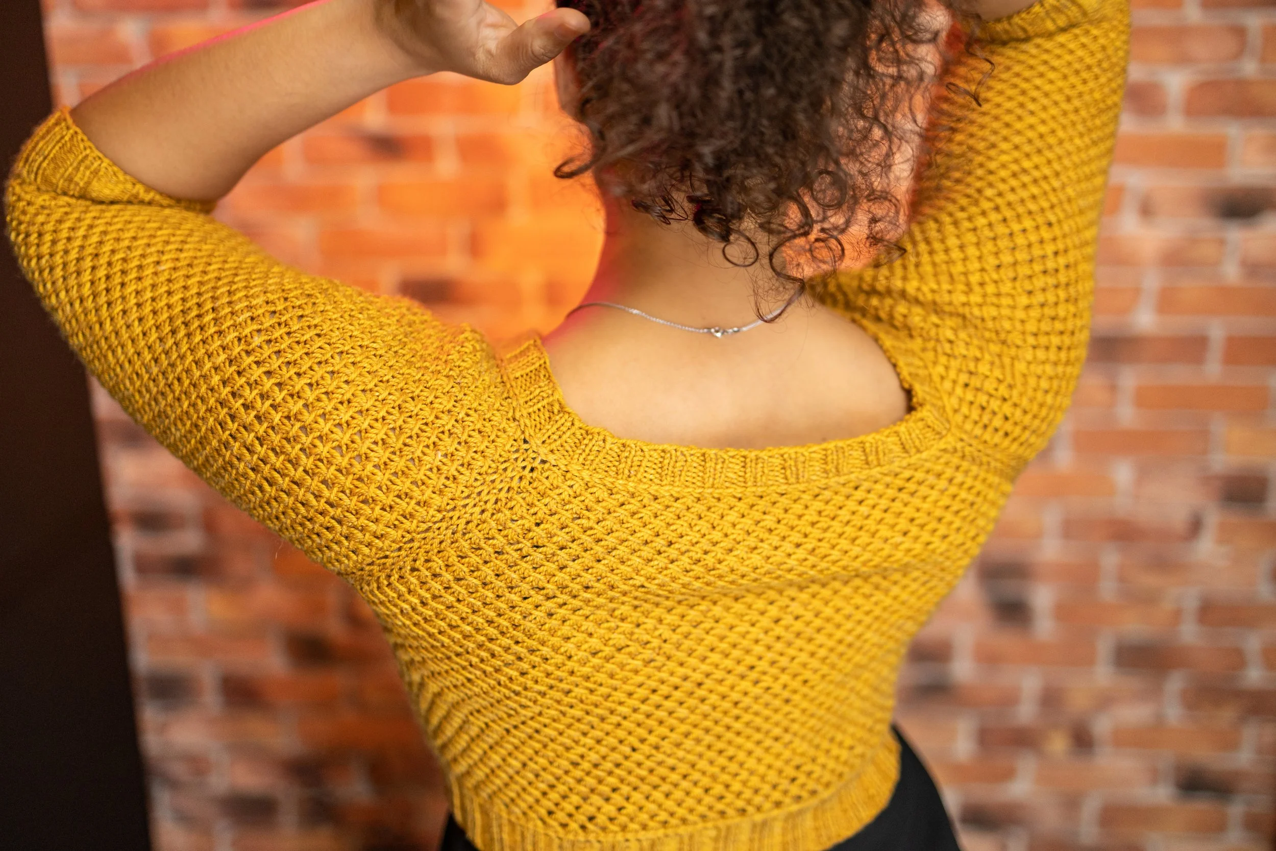 Modern knitting pattern designer Vanessa Smith shows the back of the yellow cropped-length Nydia Cardigan with 3/4 sleeves and shaped body for a close, timeless, and feminine fit. Instant PDF download
