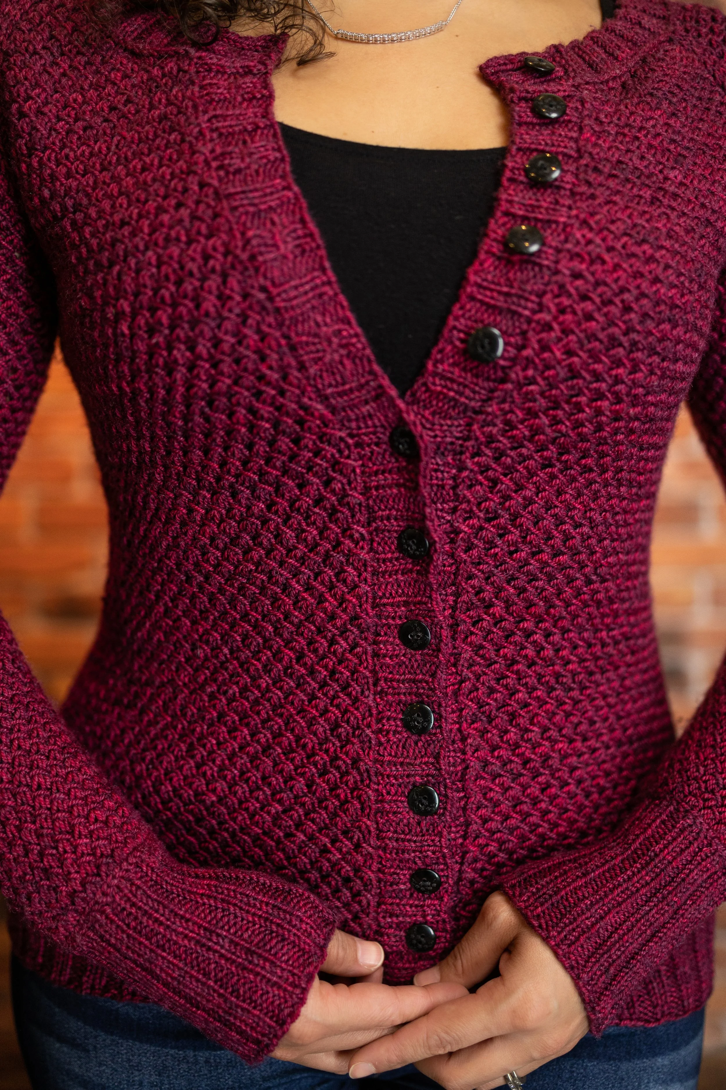 Close-up of the squishy texture and neat button band on the full-length red Nydia Cardigan. Learn how to sew buttons onto a handknit garment with this PDF knitting pattern by Vanessa Smith Designs.