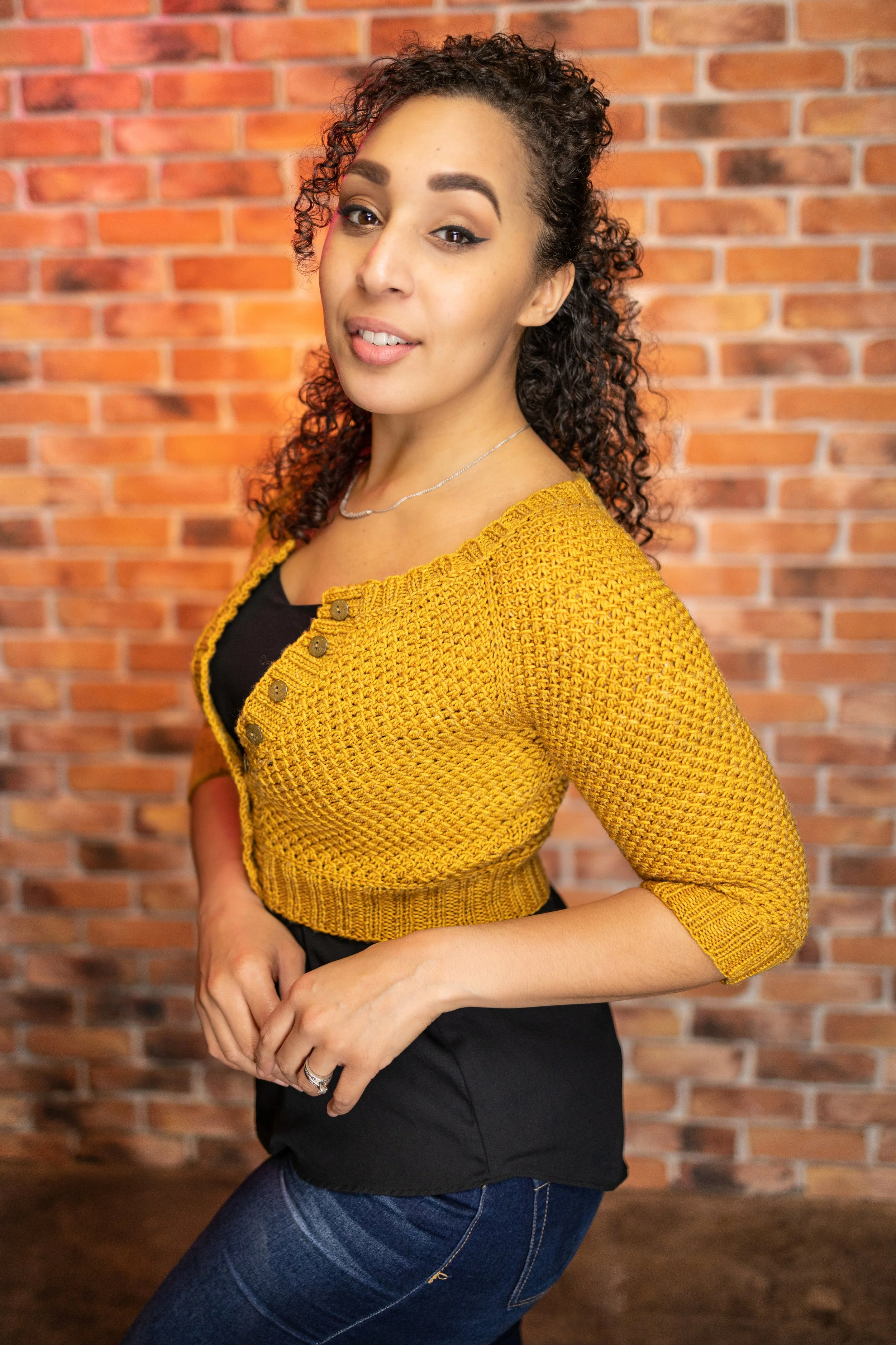 Knitting pattern designer Vanessa Smith shows a side view of her little yellow sweater, the cropped Nydia Cardigan. Tapered, 3/4 length sleeves & waist shaping elevate the fit of this top-down raglan.