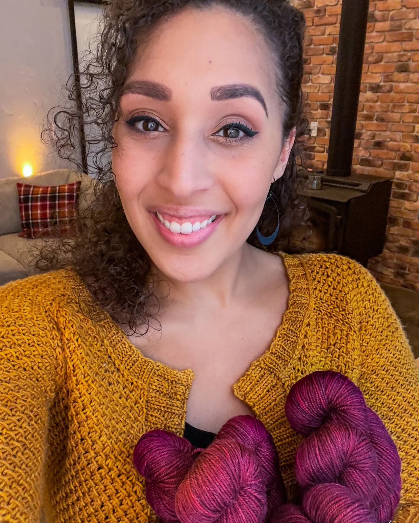 PNW-based knitwear designer Vanessa Smith wears her top-down Nydia Cardigan, handknit in a golden yellow DK weight yarn. She holds a sweater quantity of red indie, handdyed yarn for a second cardigan.