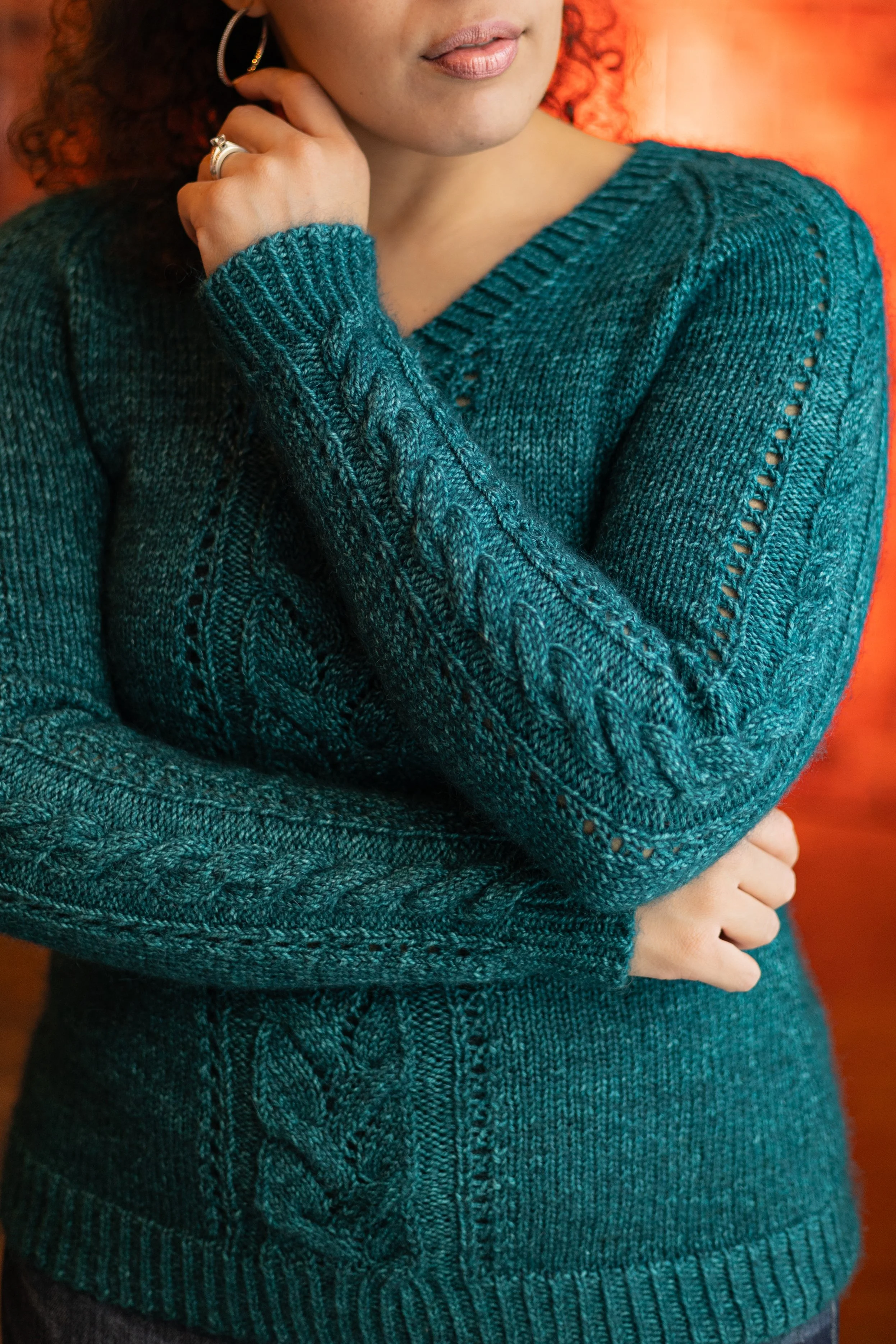 A woman looks stylish and comfortable in the handknit, teal Meant to Vee sweater, perfect for everyday elegance. Combine wool and mohair with intricate yet easy cables & lace for a cozy knit pullover.