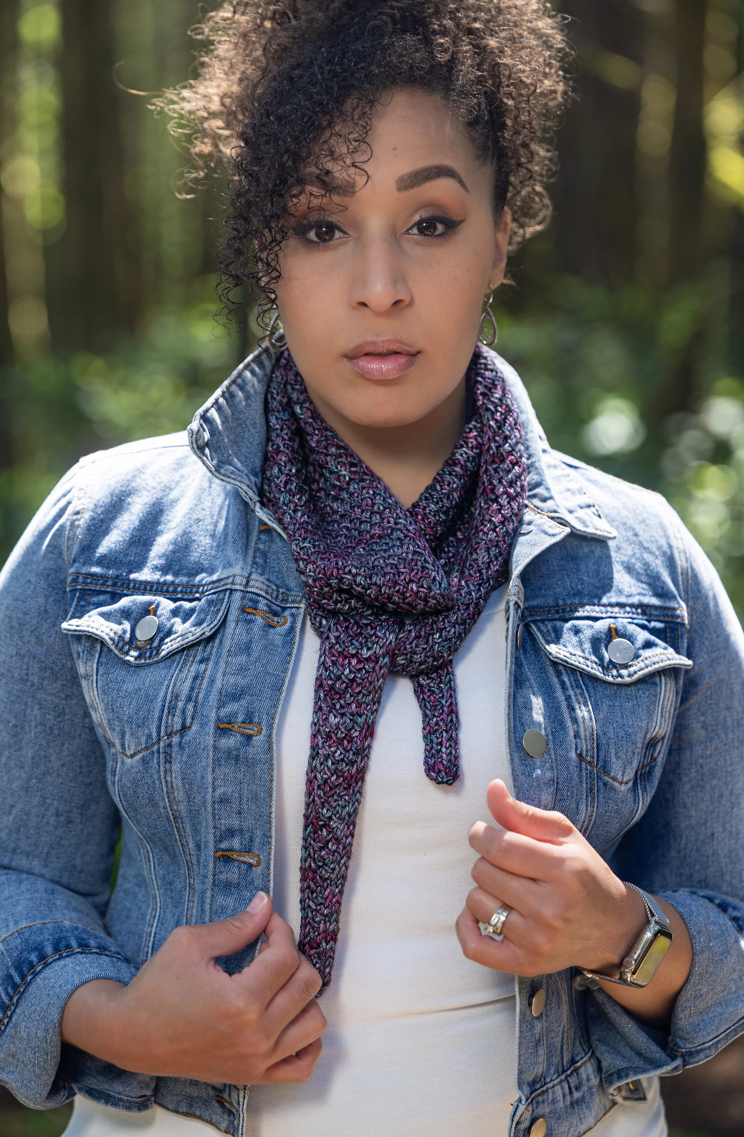 Knitwear designer Vanessa Smith wears a multicolored mini shawl named Tipping Point Scarf. Use the yarn you have with this instant download PDF knitting pattern for a stash-busting, one-skein wonder.