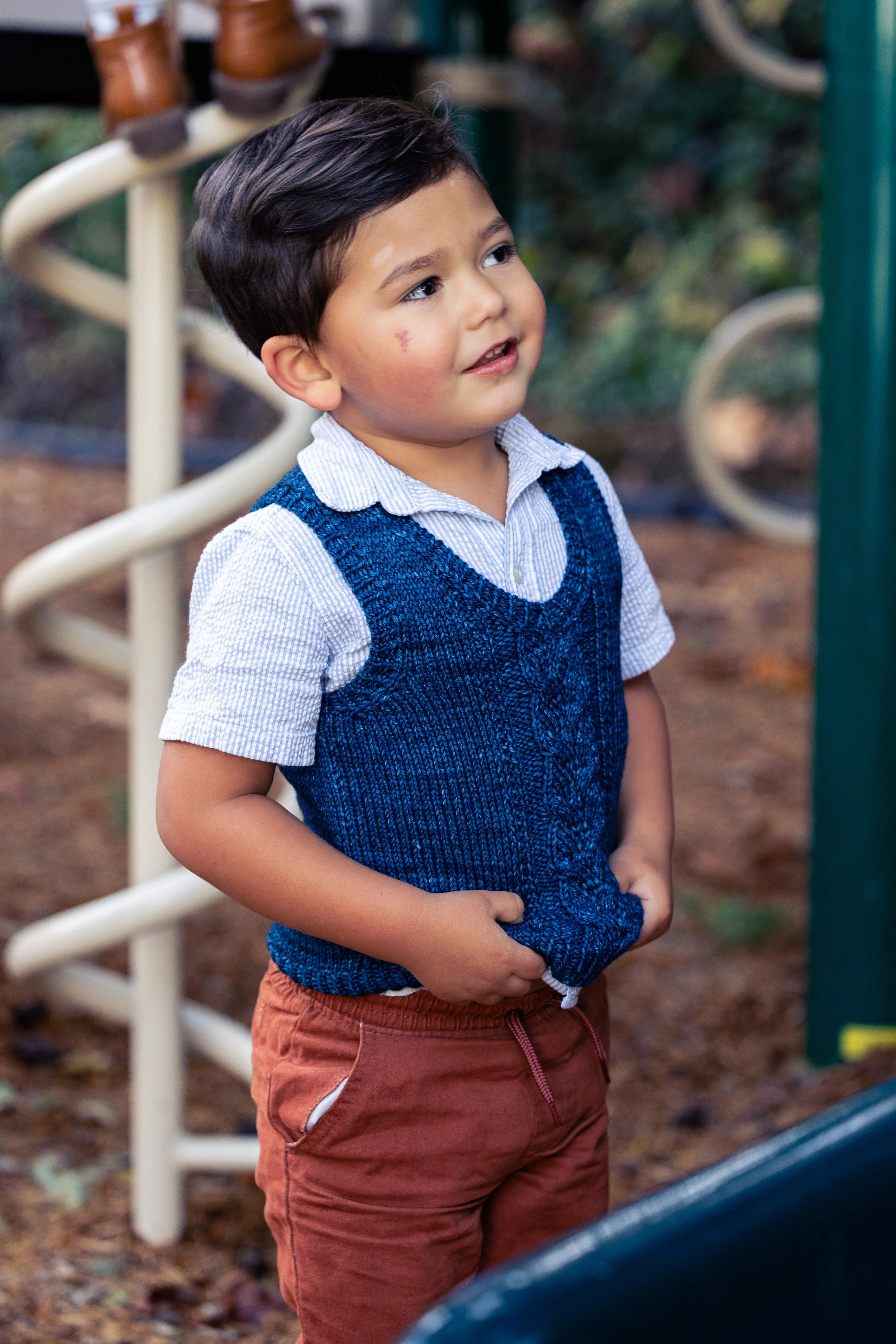 Front profile view of the Bittie Bestie Vestie, a petiteknit vest pattern designed for babies, toddlers, and children of any gender. Shown in a deep blue worsted weight yarn with cables & no yarnovers