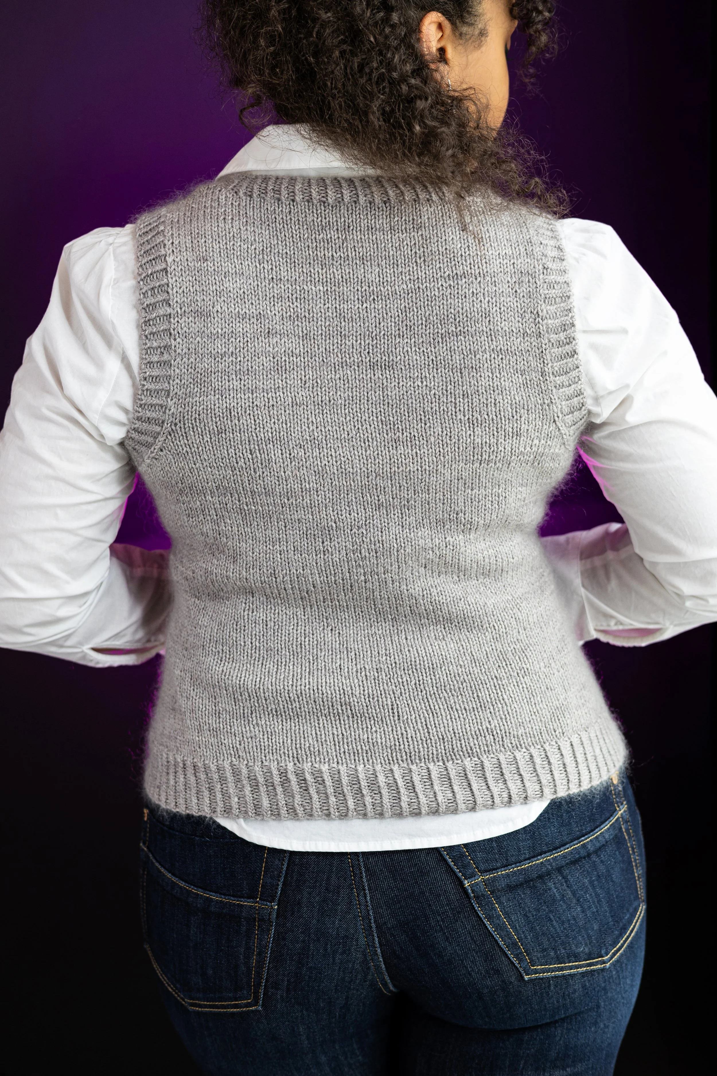 Back view of the gray hand-knitted Bestie Vestie in mid-length, highlighting the classic silhouette in this size-inclusive (petite through plus-size) digital knitting pattern by Vanessa Smith Designs.