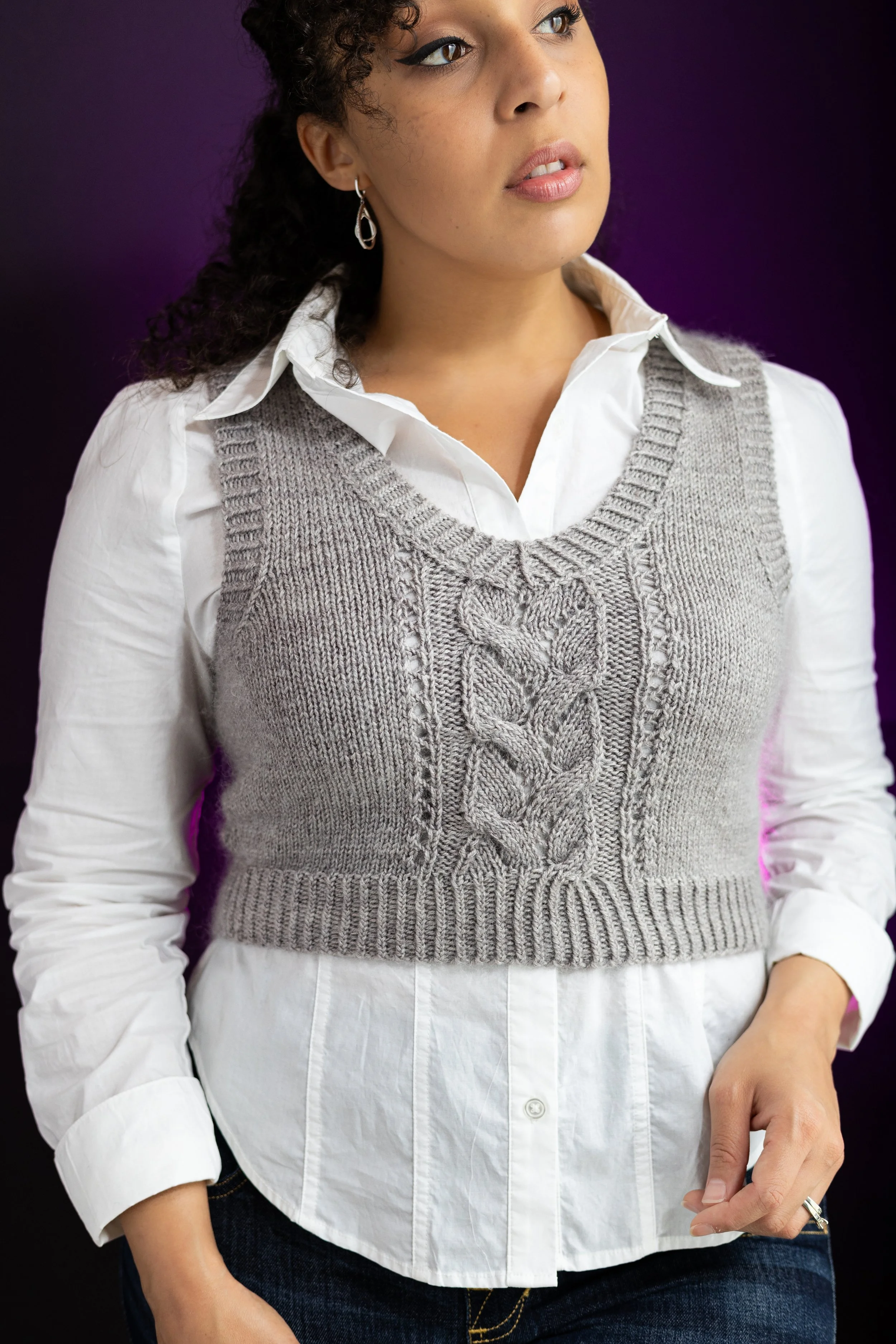 A cropped, gray Bestie Vestie knit vest styled as a versatile layer over a white button down, demonstrating its wearability. Paid women's knitting pattern for petite through plus size by Vanessa Smith