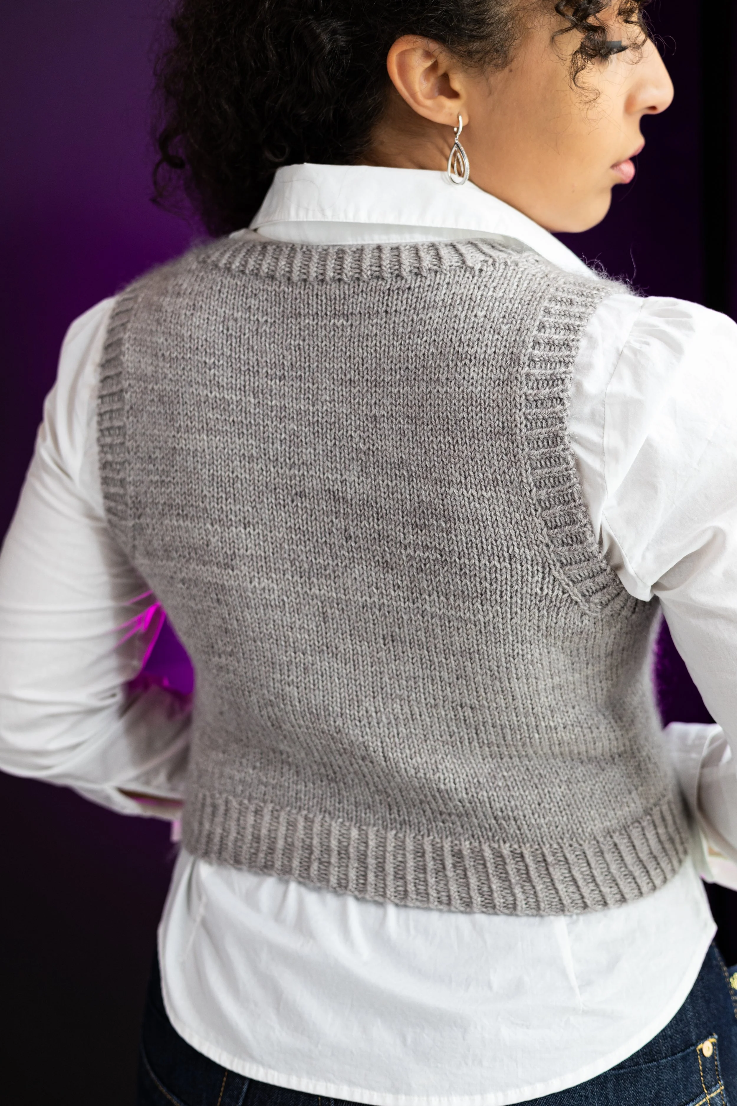 Back view of the classic gray hand-knitted Bestie Vestie in cropped length, highlighting the sweater vest's neat fit and shaping for women's sizing. Paid PDF knitting pattern by Vanessa Smith Designs.