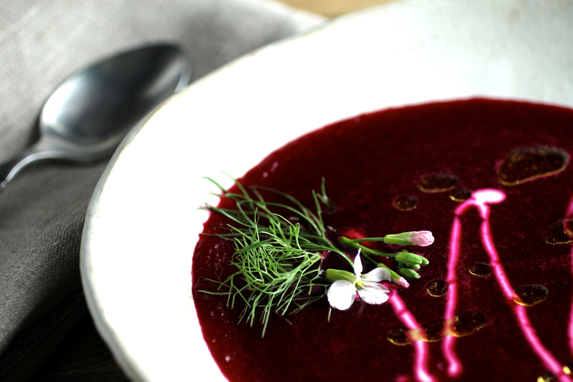 The dark red beetroot soup in this photo is complemented by radish flours, yogurt, and fennel fronds.