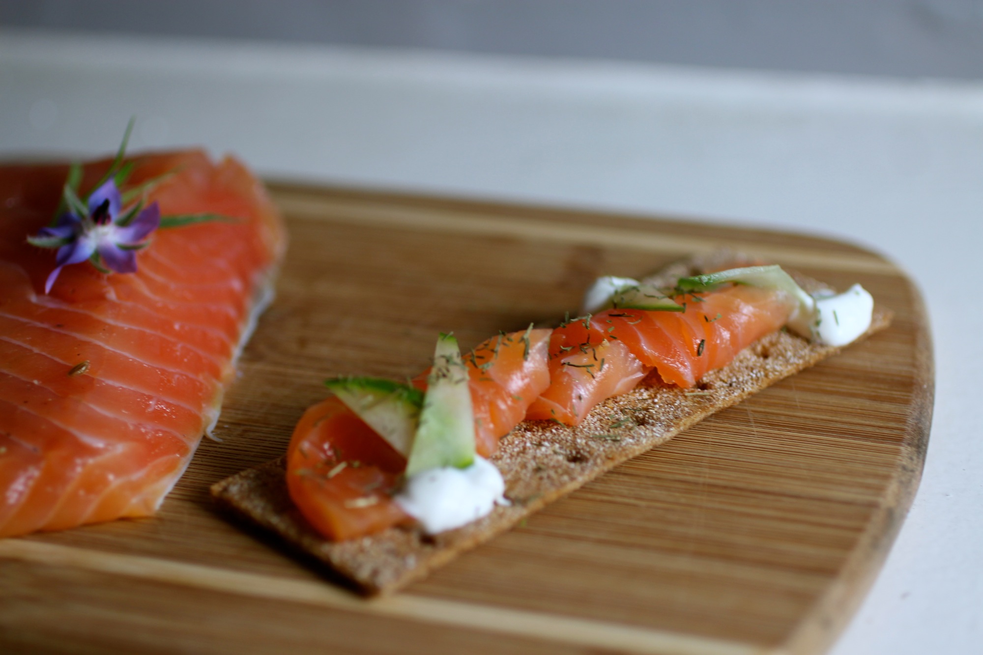 Gravlax with crème fraîche, cucumber, and dill on rye cracker.