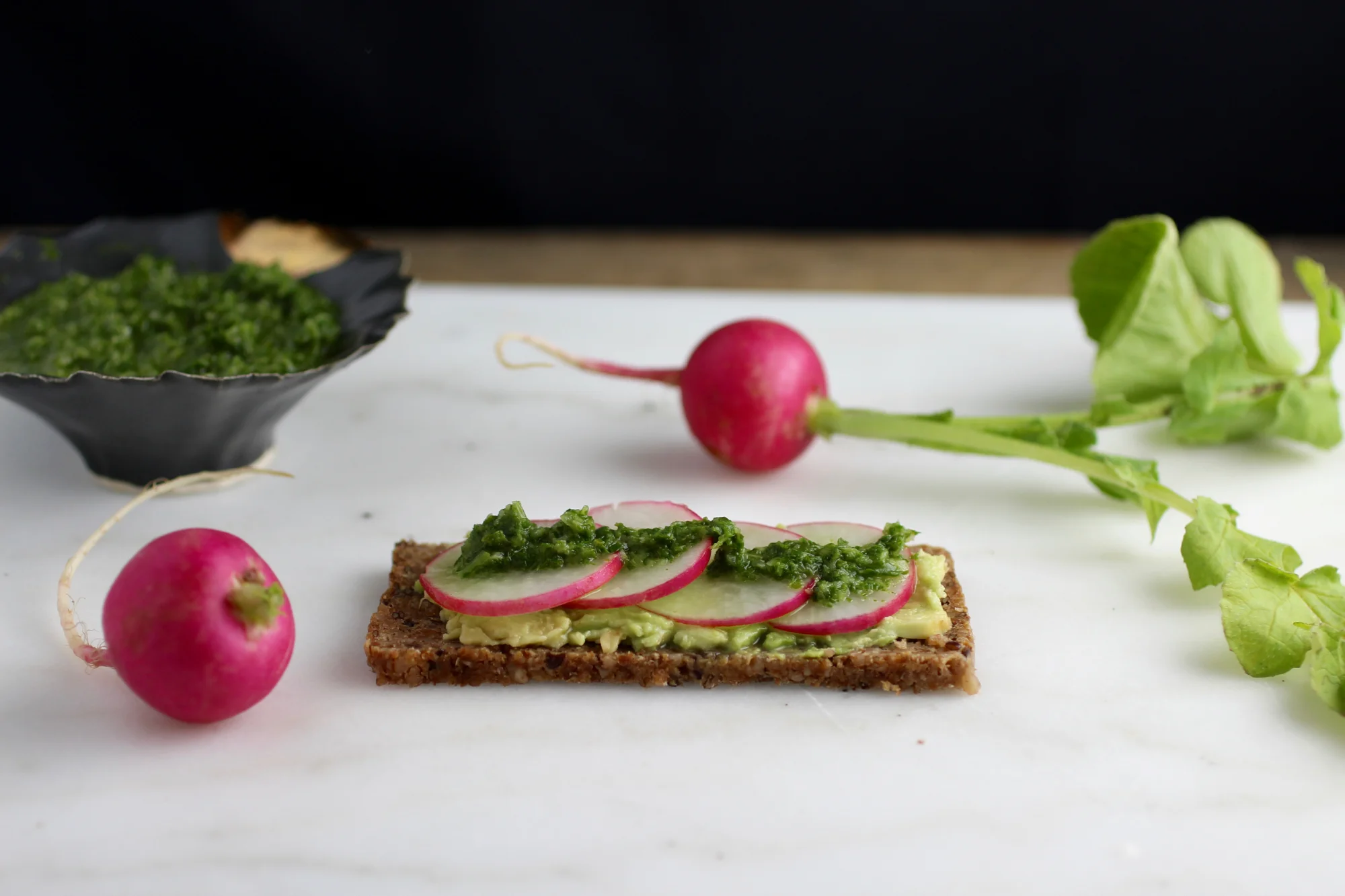 Eating "root to leaves" with sliced radish, avocado, and radish greens chimichurri rye toast.