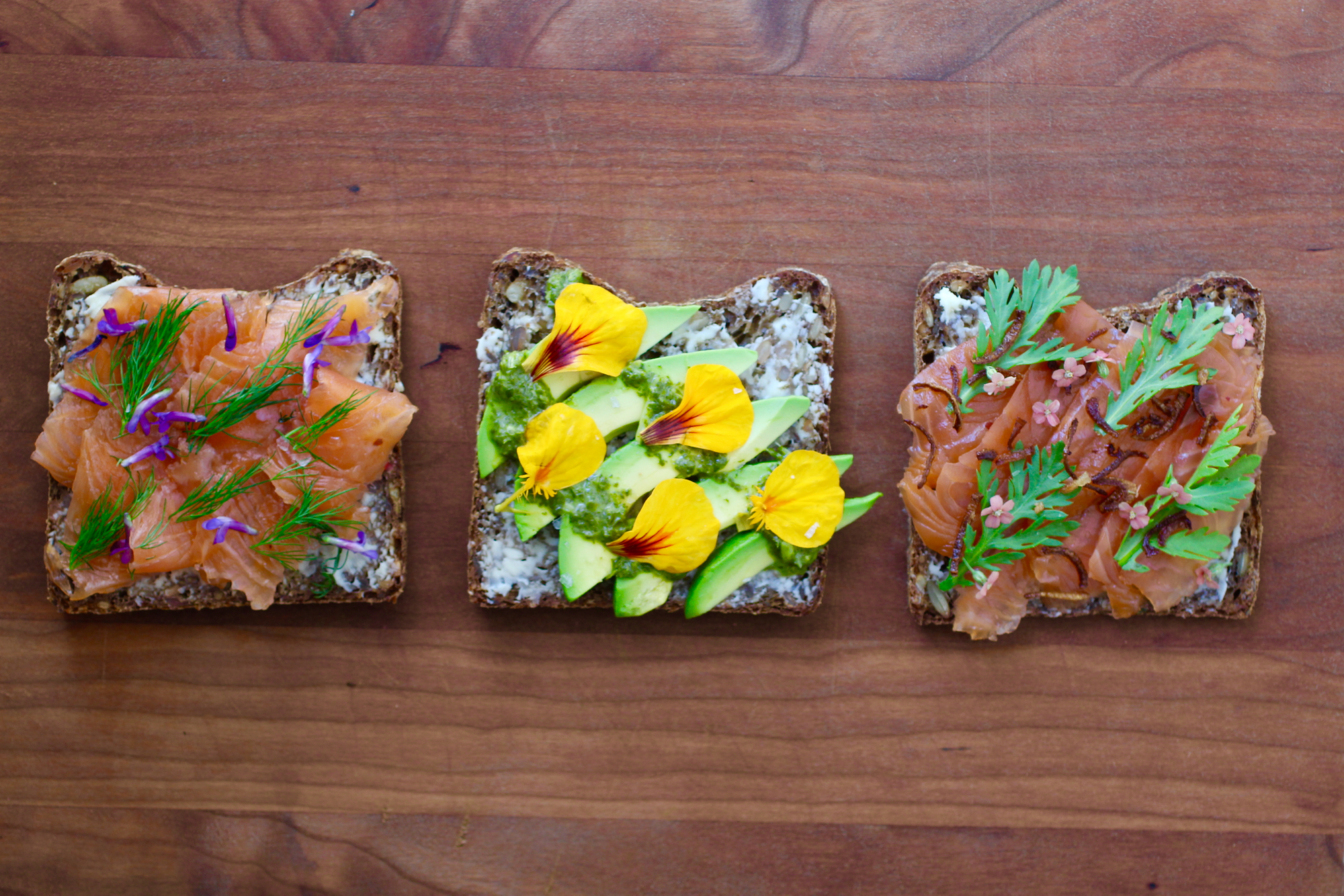 Smørrebrød topped with gravlax, dill, and foraged vetch flowers; avocado and nasturtium; and gravlax, crispy shallot, yarrow, and chrysanthemum.