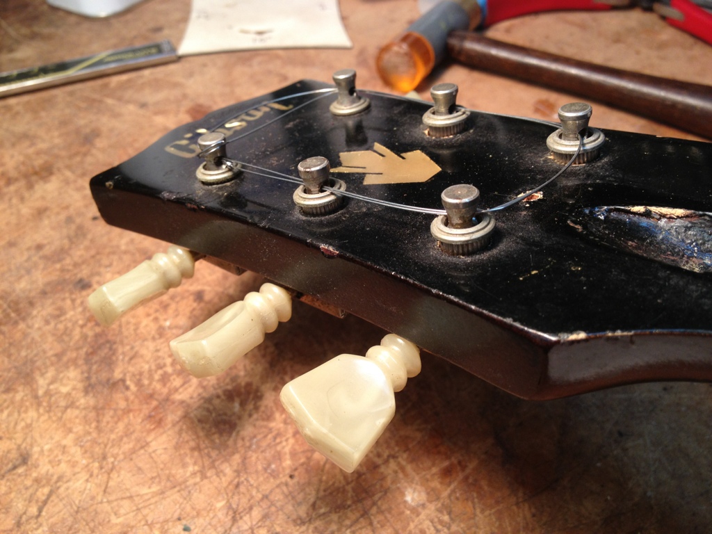 A guitar string is used to prevent the loose tuner bushings from disappearing on the shop floor.