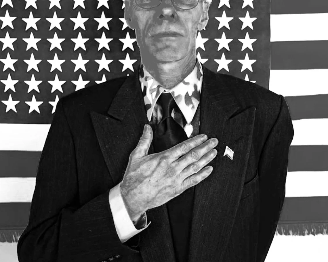 Black and white photo of a person in a suit with their hand over heart, standing in front of an American flag.