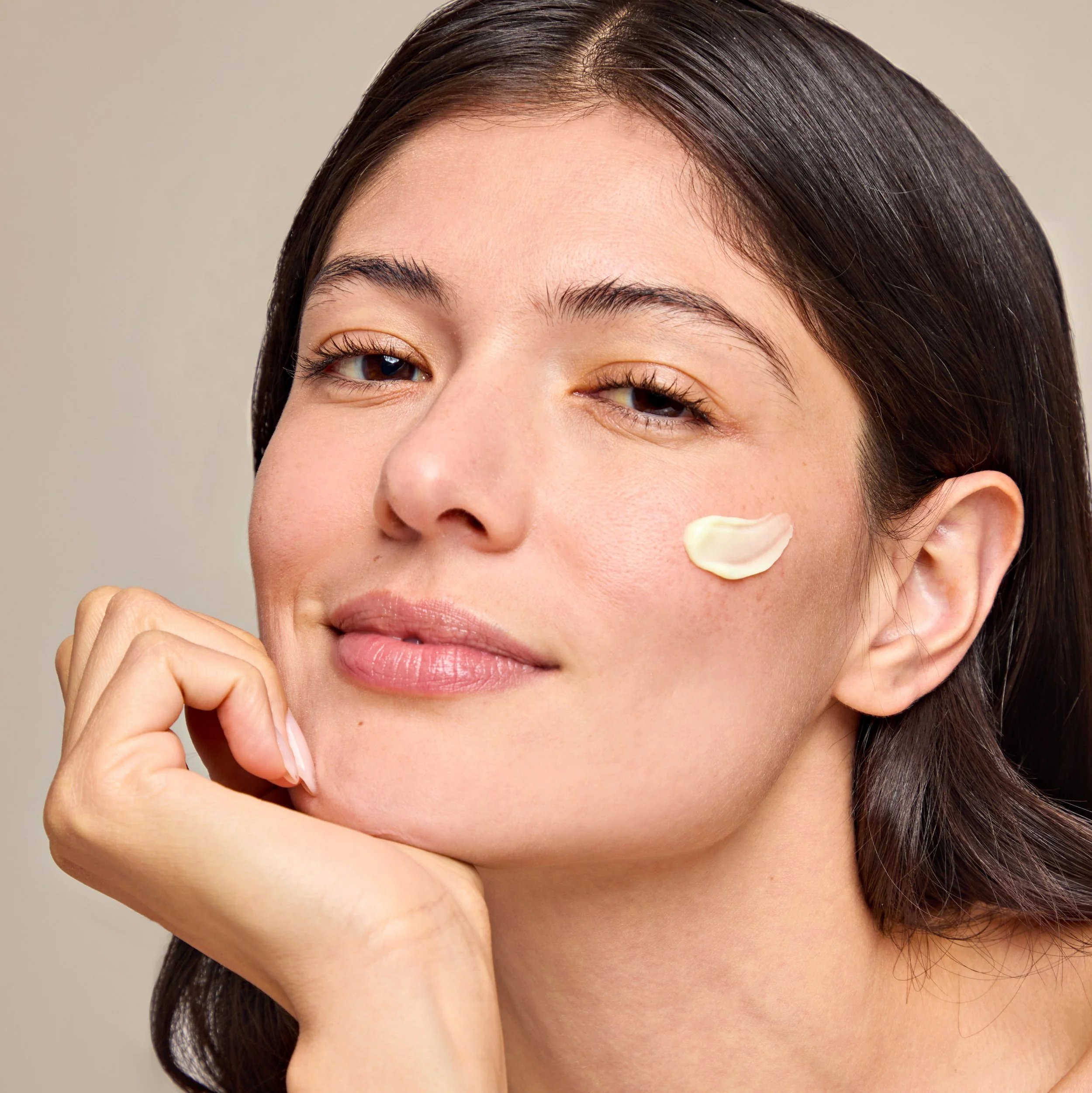 Close-up of a woman with dark hair, and clear skin, touching her face with her hand